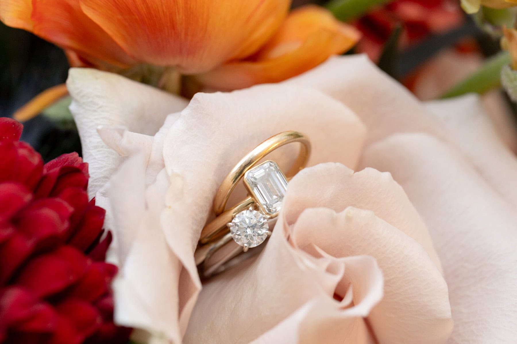 Wedding Reception at the Barker House 5 Two rings with gemstones rest on a pale pink rose, surrounded by red and orange flowers at a Barker House wedding reception.