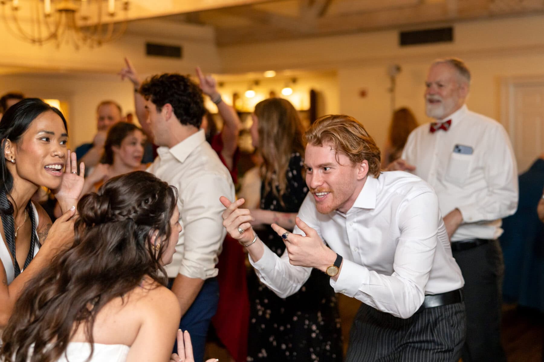 Wedding Reception at the Barker House 34 A group of people laugh and gesture while dancing together at a warmly lit Barker House wedding reception.