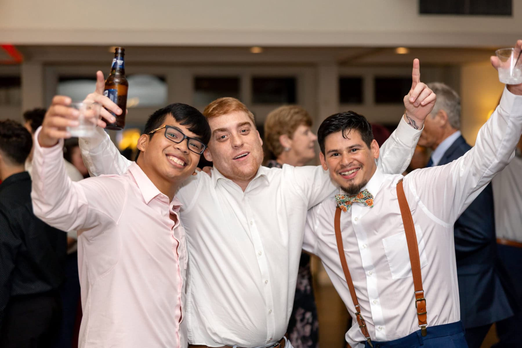 Wedding Reception at the Barker House 36 Three men in dress shirts pose together, smiling and holding drinks at a wedding reception in Barker House, with others in the background.