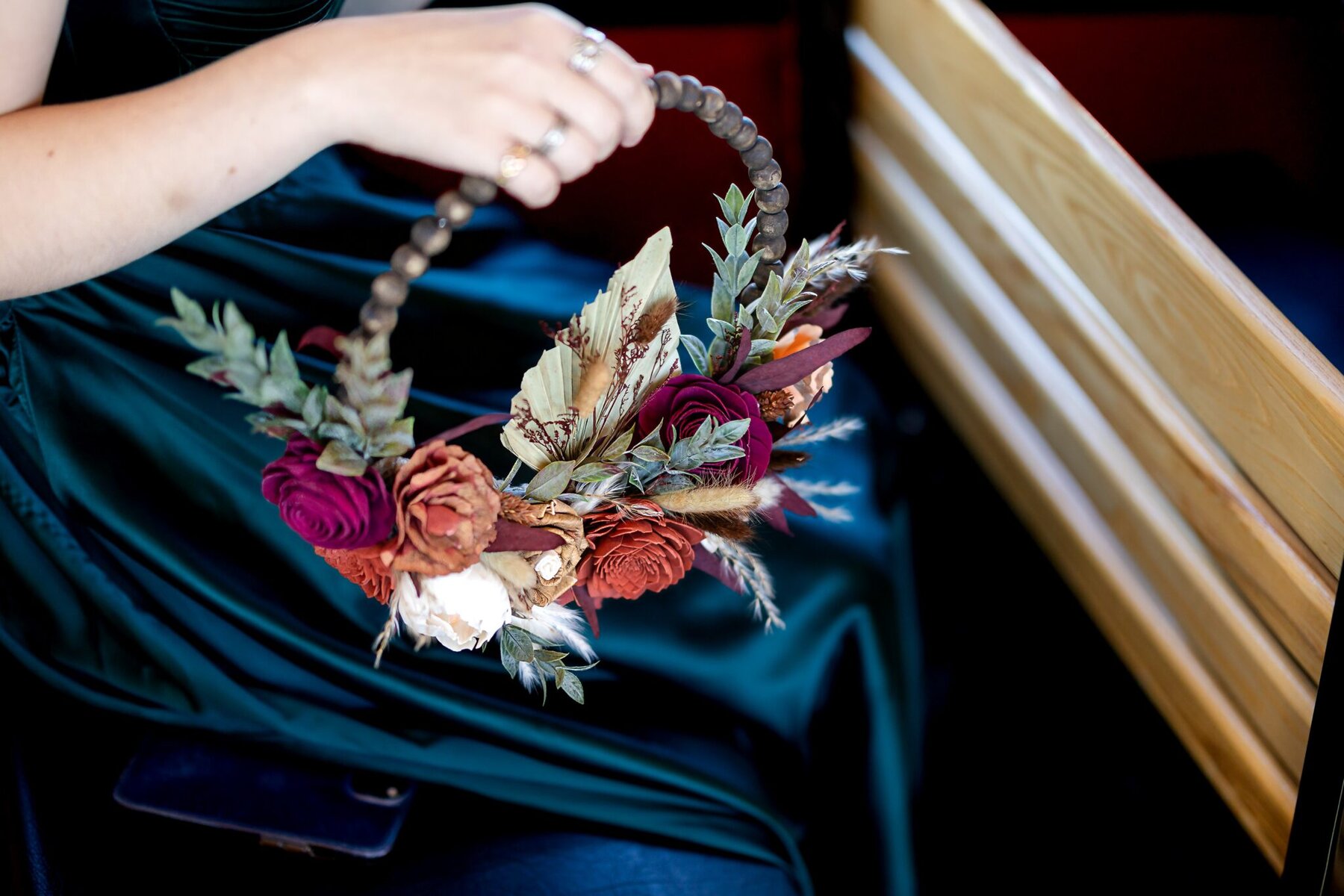 Wedding at the Newport Naval Station Officers' Club 23 A person in a dark green dress holds a floral wedding arrangement, sitting beside a wooden bench at the Newport Naval Station Officers' Club.