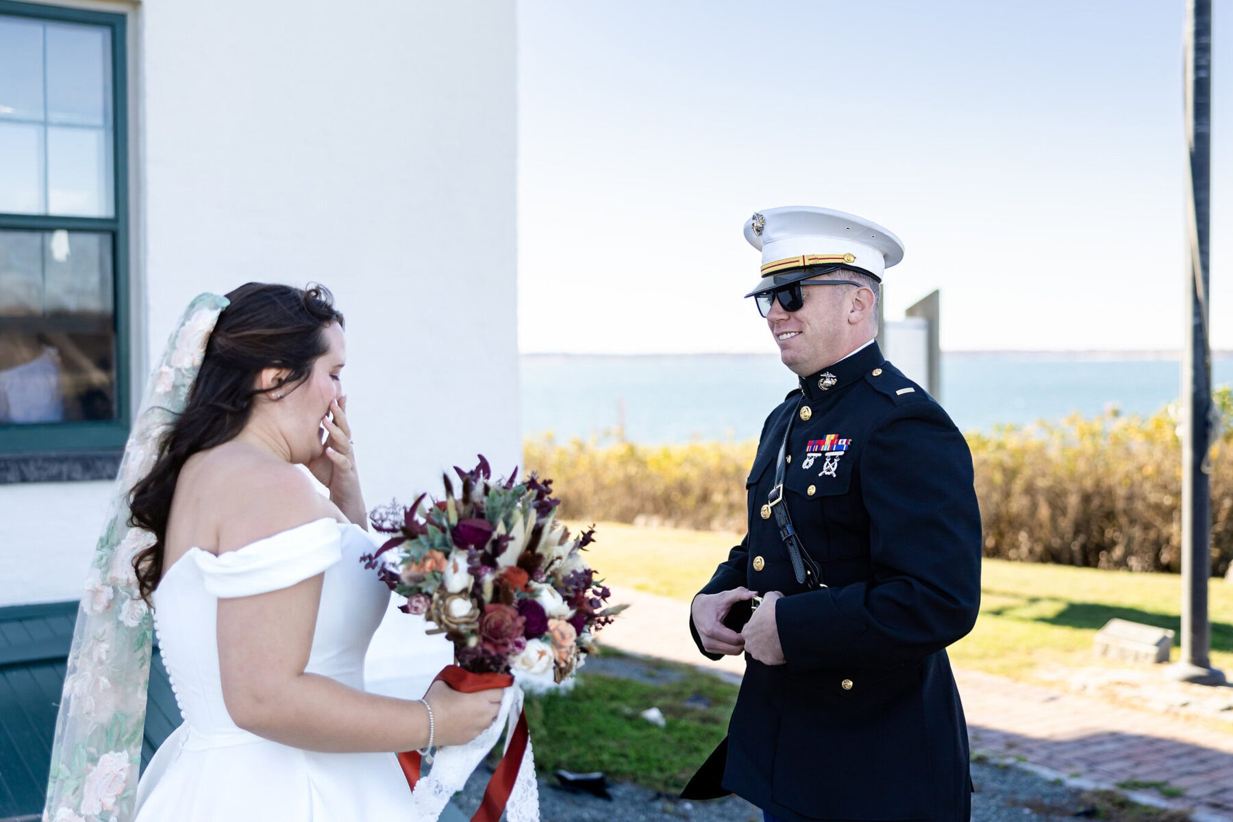 Wedding at the Newport Naval Station Officers' Club 17 A bride with a bouquet wipes her face, standing before a smiling Marine in dress uniform at a Newport Naval Station wedding by the water.