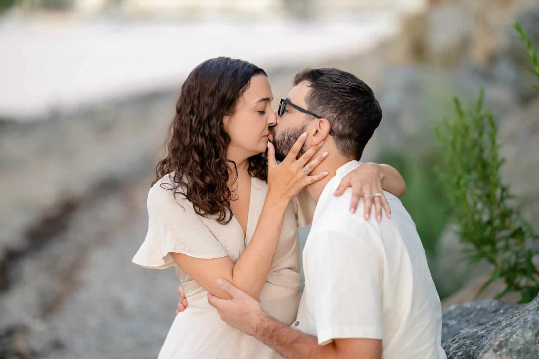 Webb Park in Weymouth, MA Engagement Session 35 A woman with curly hair gently holds a bearded man's face at Webb Park in Weymouth MA during their engagement session, sitting closely together outdoors, affectionate and intimate.