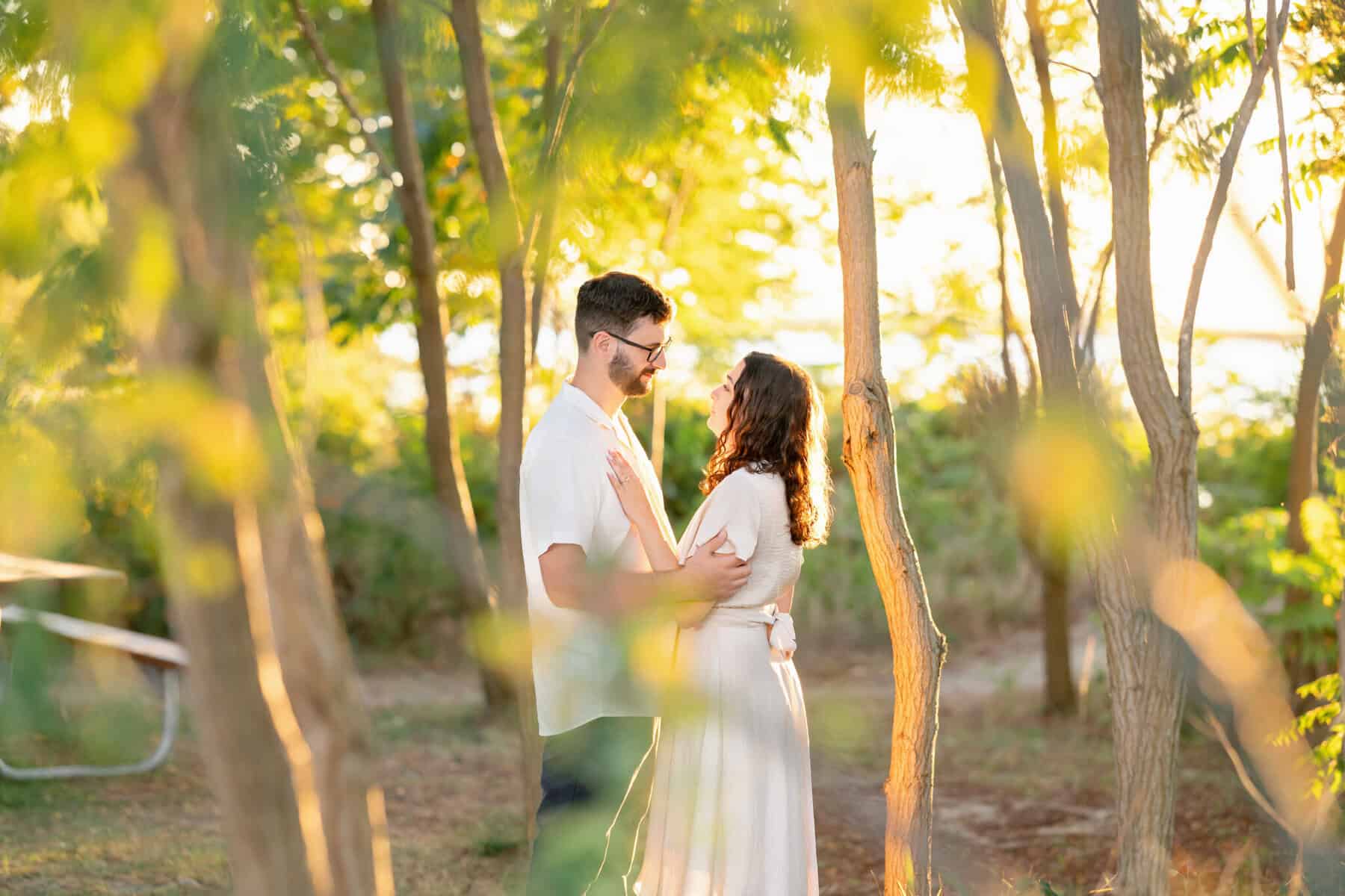 Webb Park in Weymouth, MA Engagement Session 5 A couple stands close together in sunlit Webb Park, Weymouth MA, gazing at each other lovingly. Sunlight filters through the trees, creating a warm, romantic engagement session atmosphere.