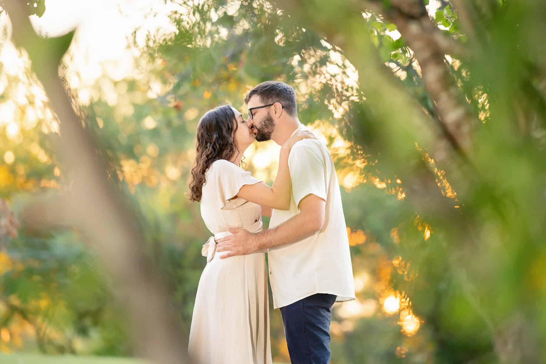 Webb Park in Weymouth, MA Engagement Session 19 A couple shares a kiss amid green foliage and soft sunlight at Webb Park in Weymouth MA during their engagement session.
