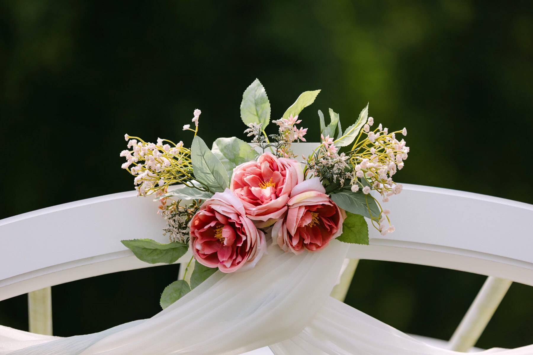 Wedding At the Holliston Historical Society 3 Pink and white artificial flowers adorn a white chair at a Holliston Historical Society wedding venue, set against a blurred green background.