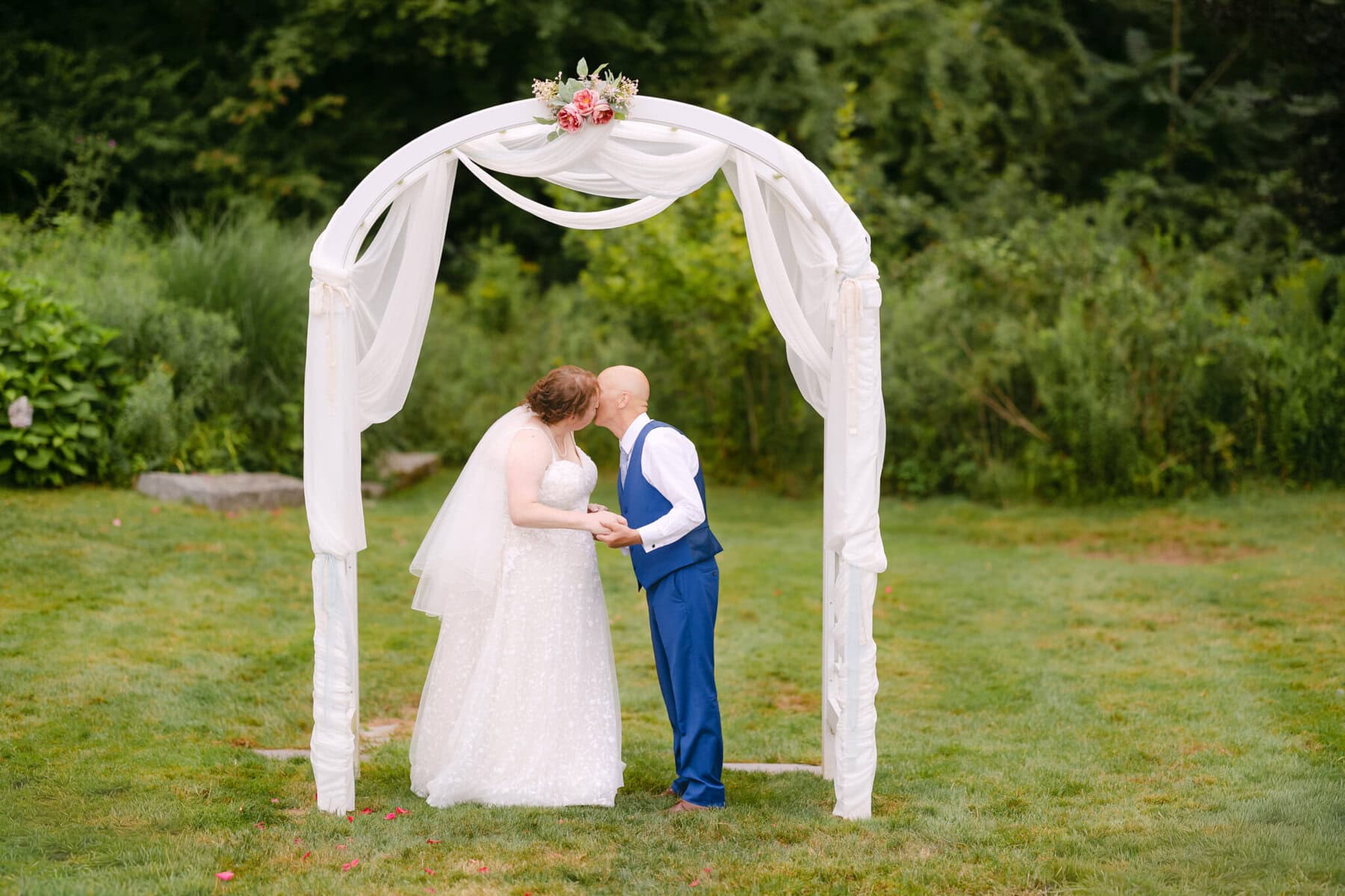 Wedding At the Holliston Historical Society 61 A man and woman sharing a wedding kiss under a white arch at the Holliston Historical Society.