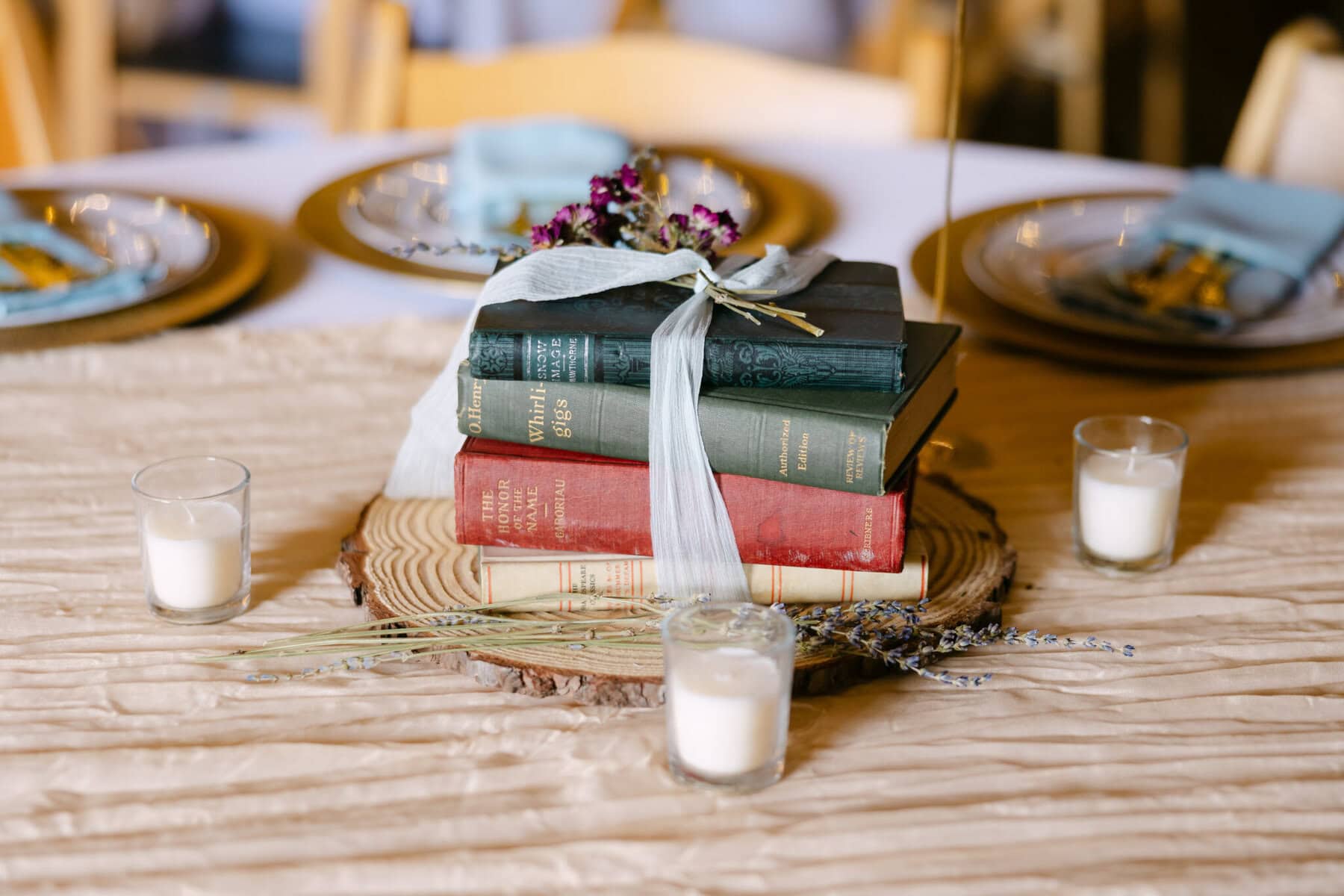 Wedding At the Holliston Historical Society 34 A stack of books tied with a ribbon sits on a wood slice, surrounded by candles and lavender at a Holliston Historical Society wedding table.