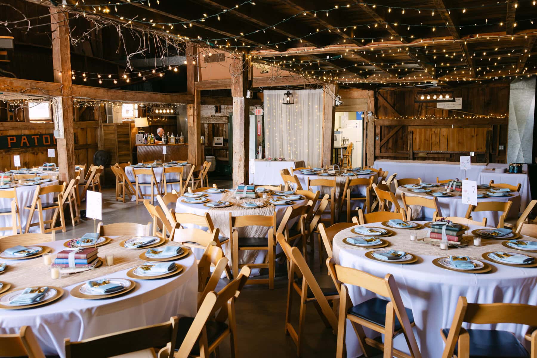 Wedding At the Holliston Historical Society 36 A rustic event hall at the Holliston Historical Society with round tables, wooden chairs, string lights—perfect for a charming wedding celebration.