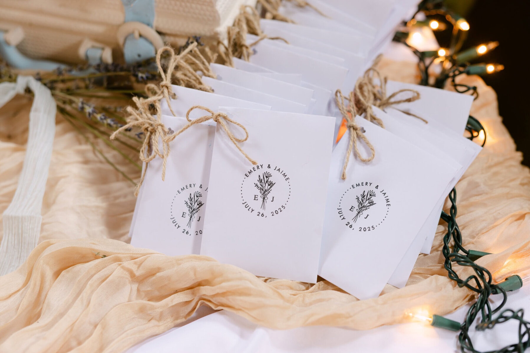 Wedding At the Holliston Historical Society 30 A row of white paper wedding packets tied with twine, labeled with "E&M" and date, displayed at Holliston Historical Society with string lights.