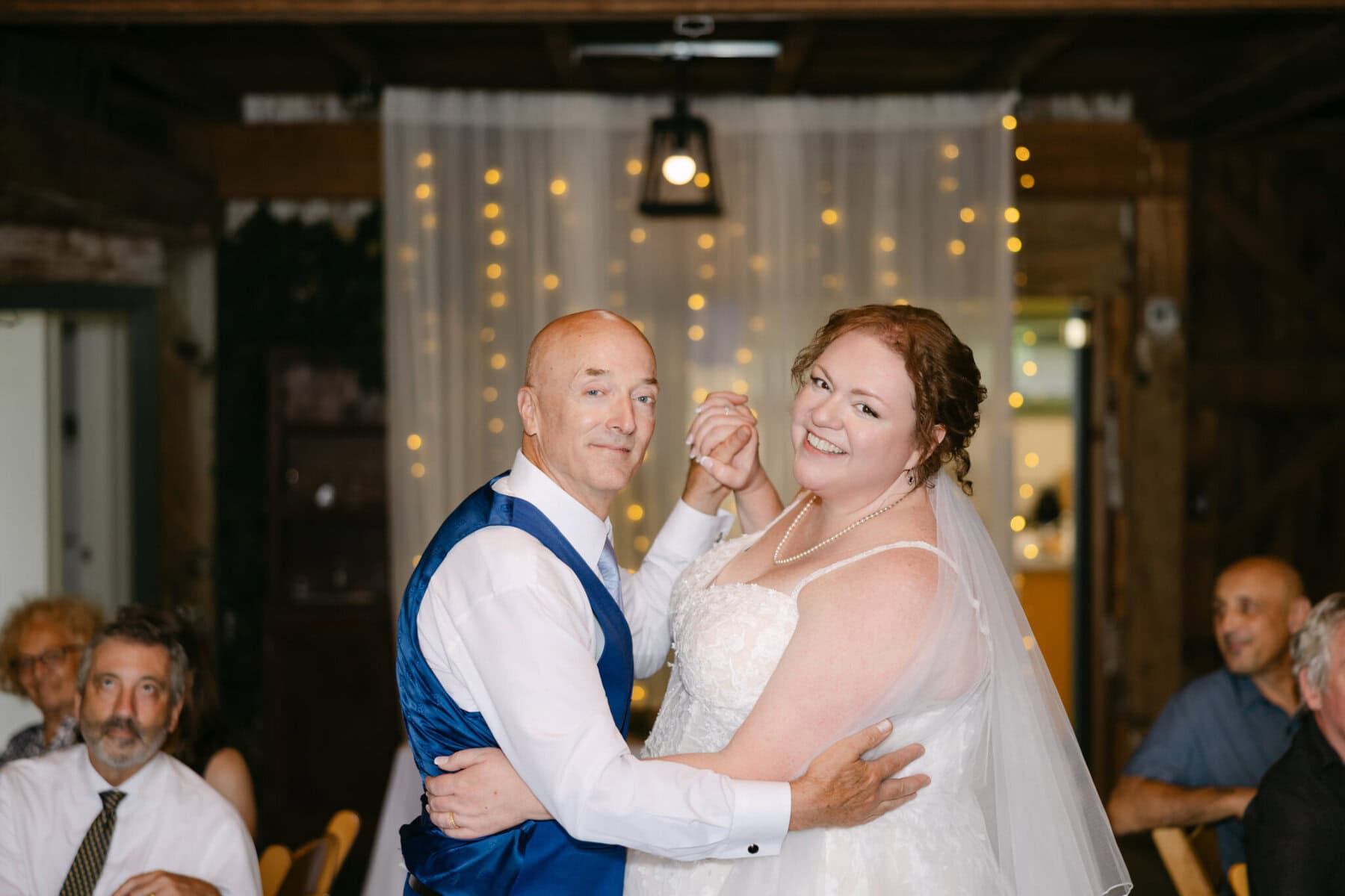 Wedding At the Holliston Historical Society 44 A bride in a white dress and veil dances with a man at a wedding reception at the Holliston Historical Society, guests seated behind them.