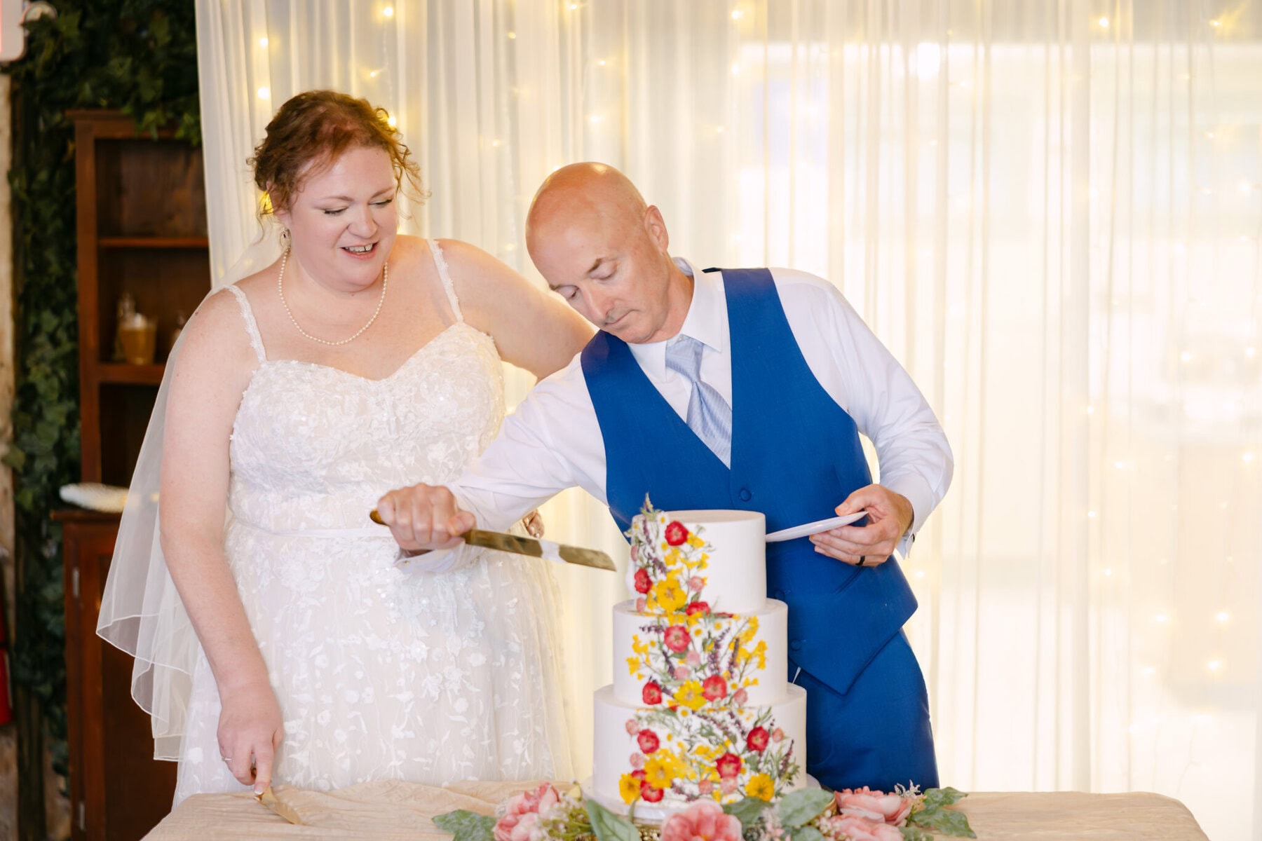 Wedding At the Holliston Historical Society 48 A bride and groom cut a white, three-tiered wedding cake at the Holliston Historical Society wedding.