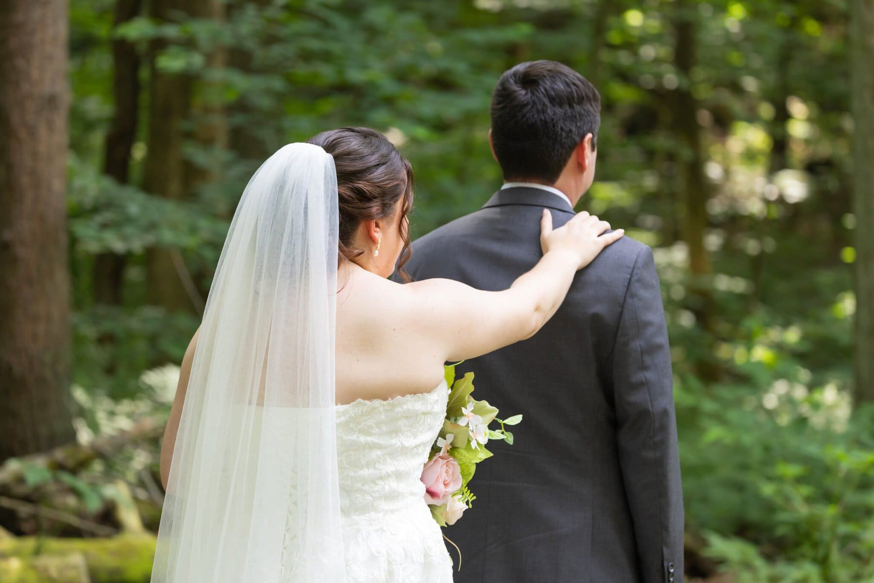 Stunning Wedding at Indian Ranch and Samuel Slater's Restaurant 15 A bride in a white dress touches the groom's shoulder at their wedding, standing outdoors near trees at Samuel Slater's Restaurant.