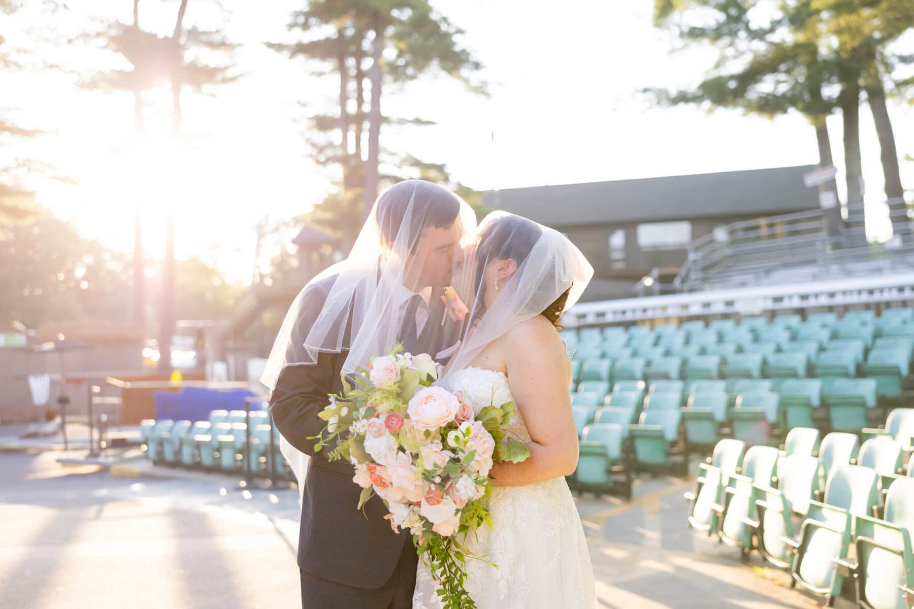 Stunning Wedding at Indian Ranch and Samuel Slater's Restaurant 53 A bride and groom share a kiss beneath their veils at Samuel Slater's Restaurant, sunlight glowing over their wedding ceremony’s empty seats.