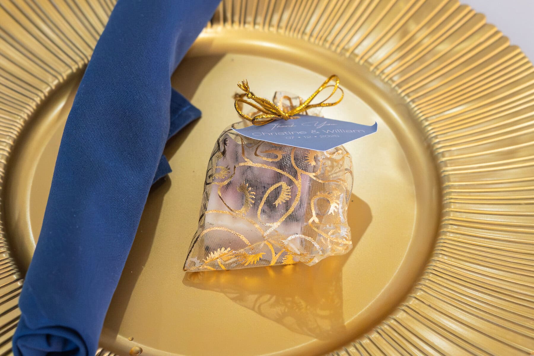 Stunning Wedding at Indian Ranch and Samuel Slater's Restaurant 72 A gold plate with a blue napkin and a sheer gold gift bag, perfect for a wedding at Samuel Slater's Restaurant or Indian Ranch.