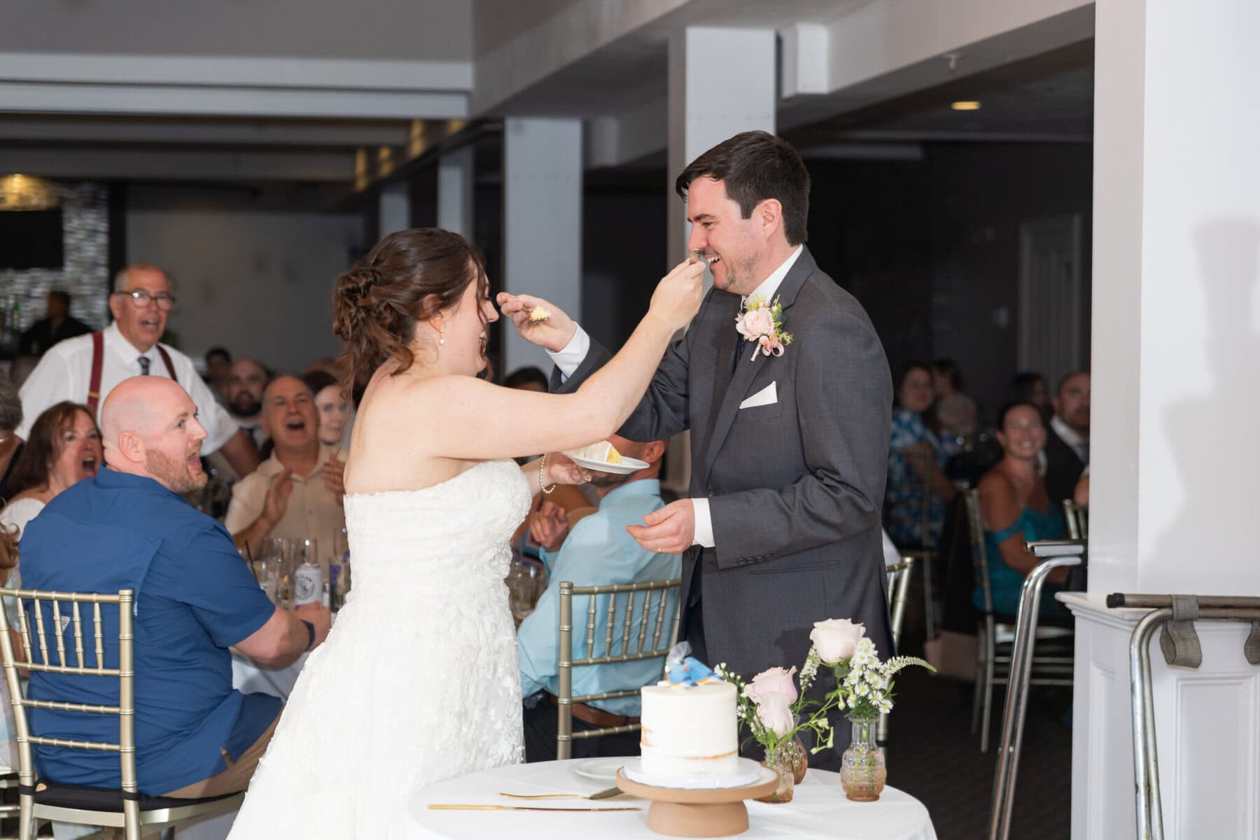 Stunning Wedding at Indian Ranch and Samuel Slater's Restaurant 86 A bride in a white dress feeds cake to her groom at an Indian Ranch wedding, as smiling guests look on in the festive reception.