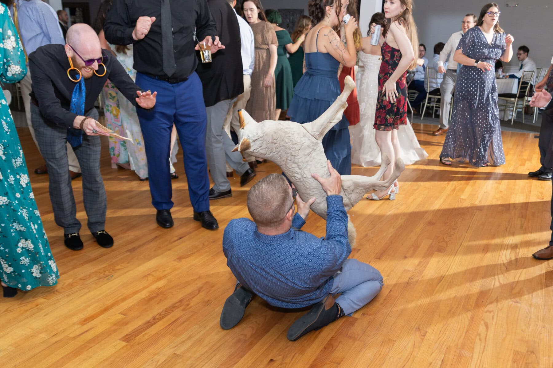 Stunning Wedding at Indian Ranch and Samuel Slater's Restaurant 99 At a lively wedding at Samuel Slater's Restaurant, a man holding a fake goat entertains as guests in formal attire dance and watch.