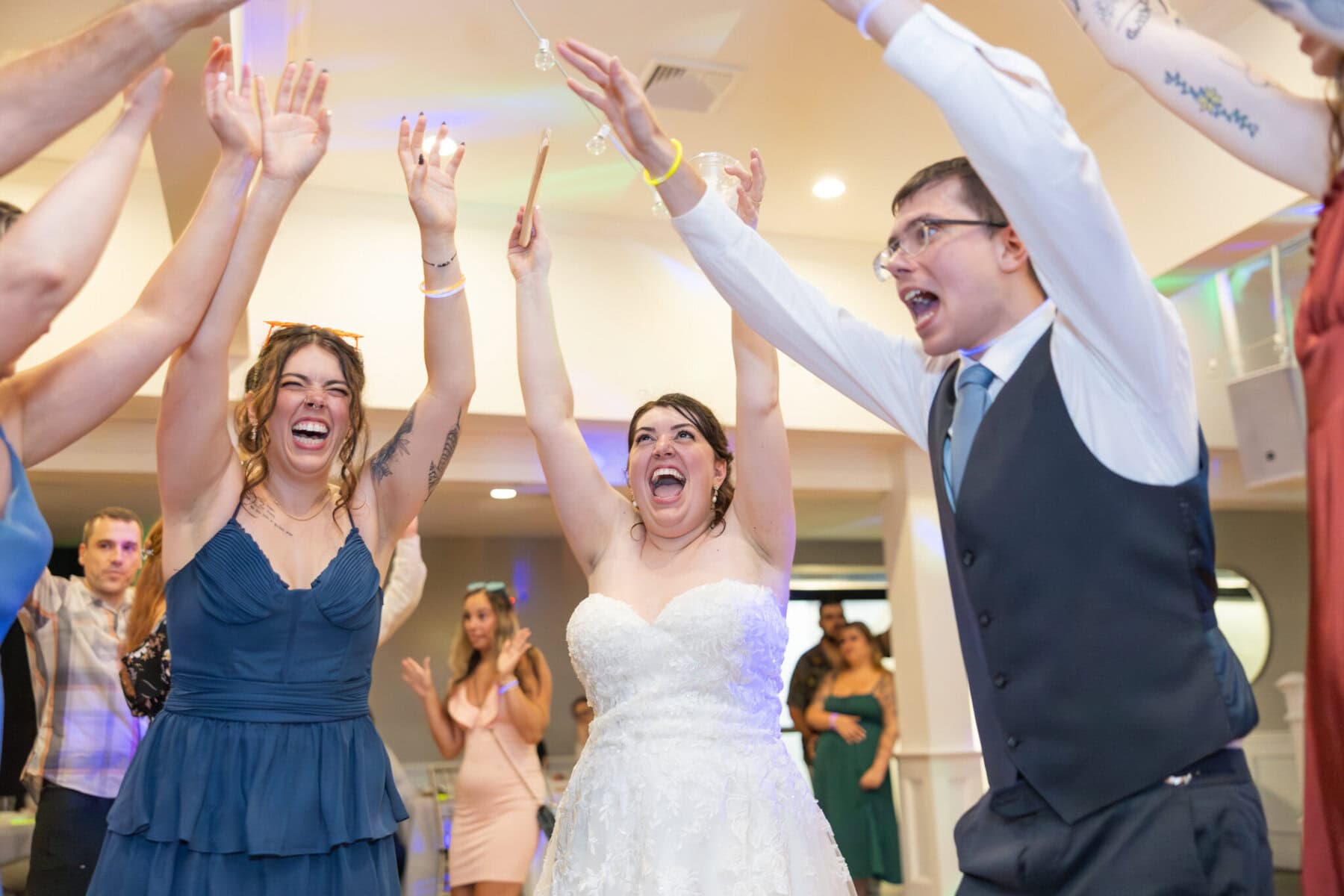 Stunning Wedding at Indian Ranch and Samuel Slater's Restaurant 106 A bride in a white dress raises her arms and smiles at her wedding, surrounded by joyful guests at Samuel Slater's Restaurant.