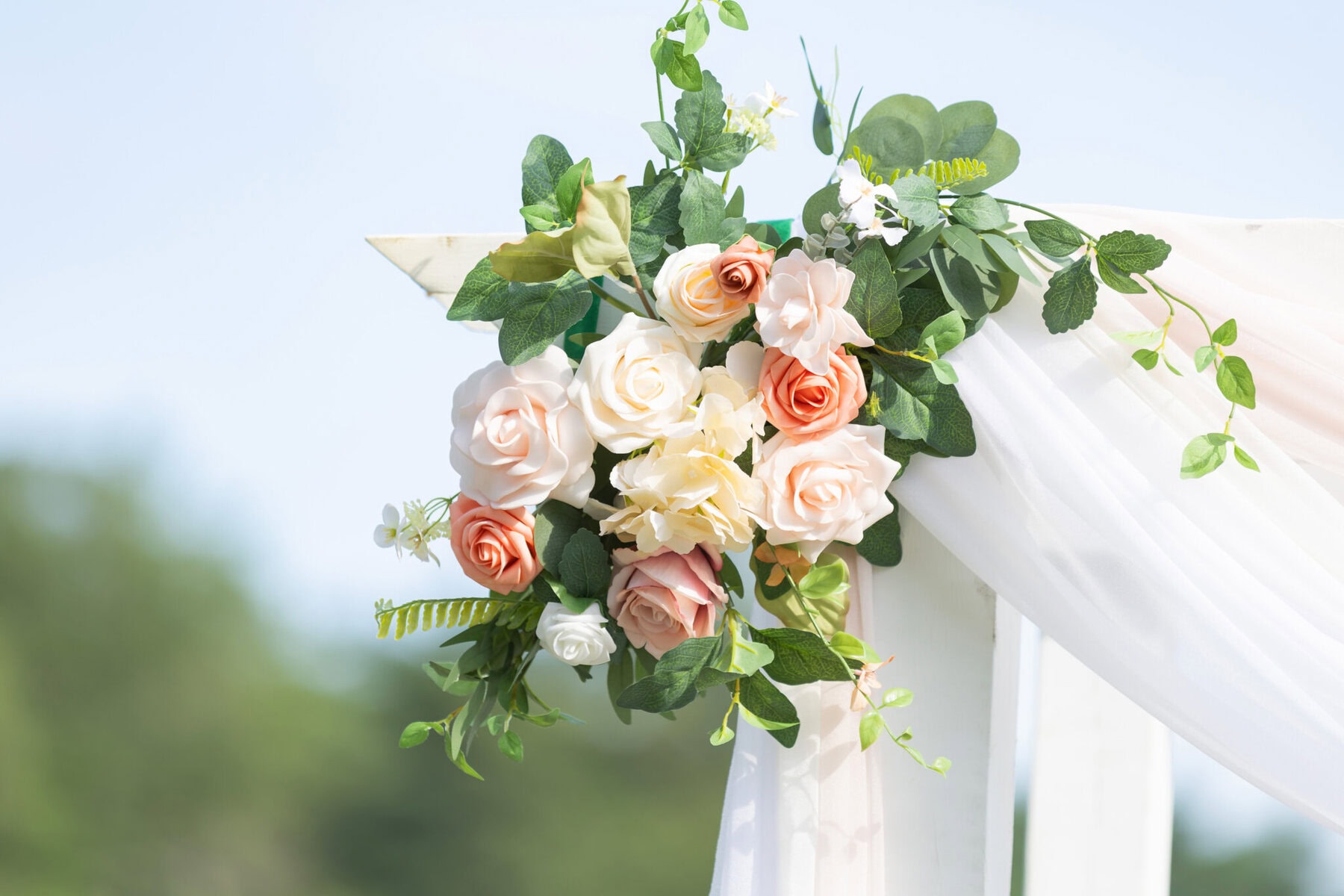 Stunning Wedding at Indian Ranch and Samuel Slater's Restaurant 26 A close-up of a wedding floral arrangement with pink, white, and peach roses on a white fabric-draped outdoor structure at Indian Ranch.