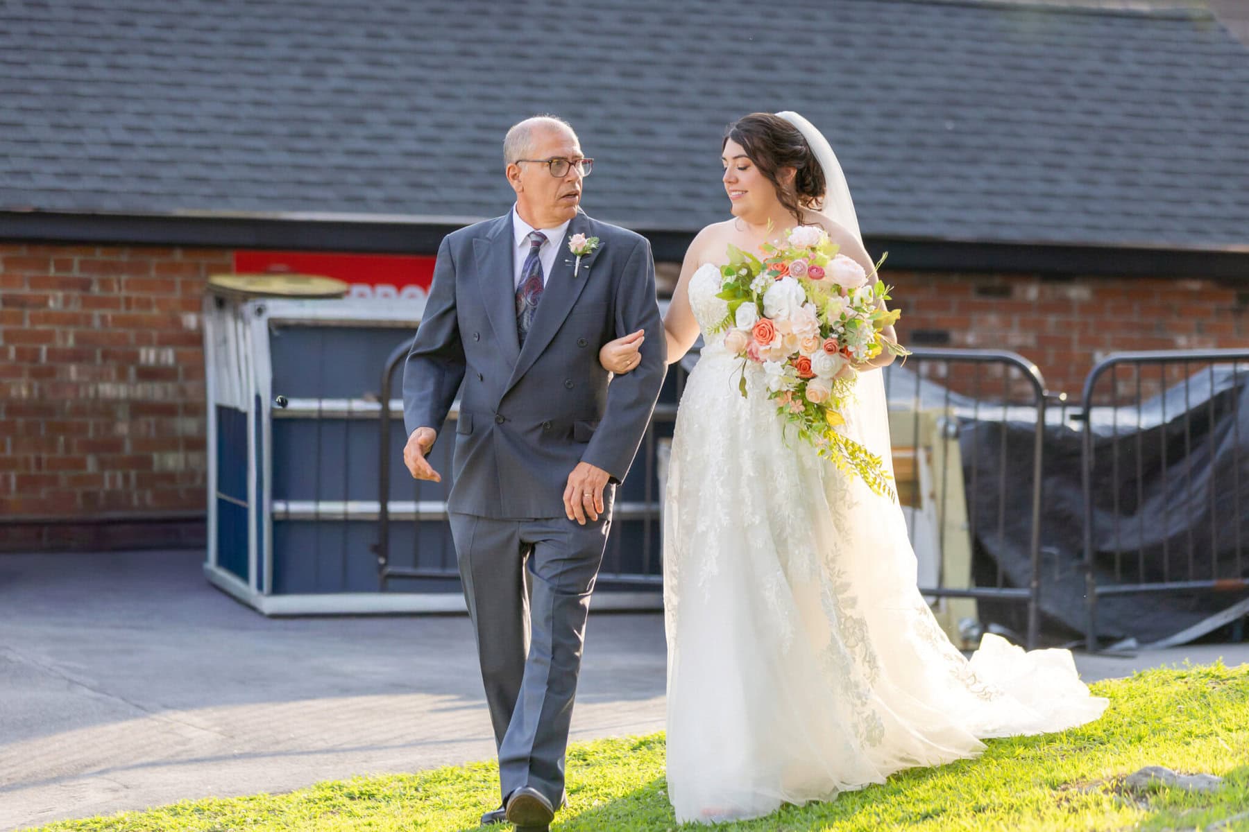 Stunning Wedding at Indian Ranch and Samuel Slater's Restaurant 34 A bride in a white dress walks outside at the Indian Ranch wedding venue, holding a bouquet and arm-in-arm with an older man in gray.