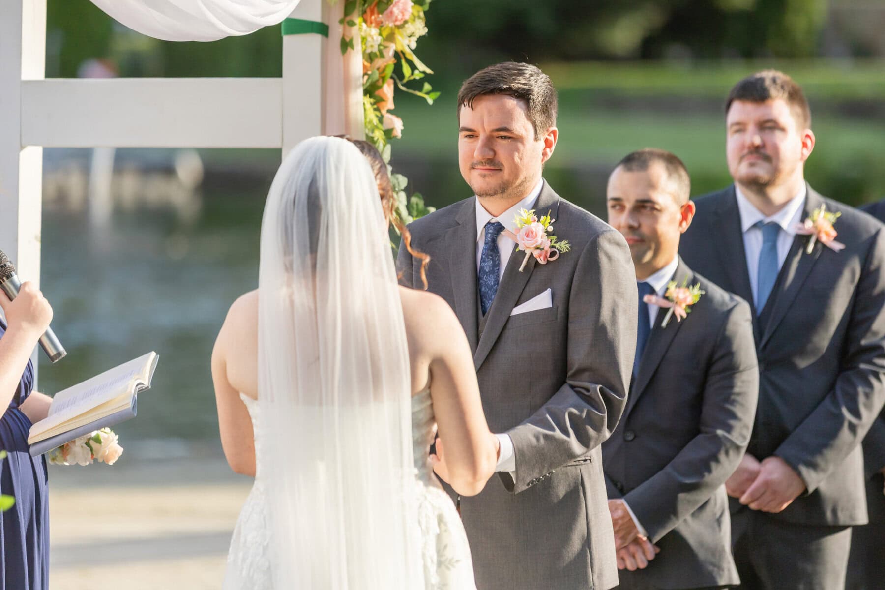 Stunning Wedding at Indian Ranch and Samuel Slater's Restaurant 39 A bride and groom stand facing each other at an outdoor wedding ceremony at Samuel Slater's Restaurant, with groomsmen and an officiant nearby.