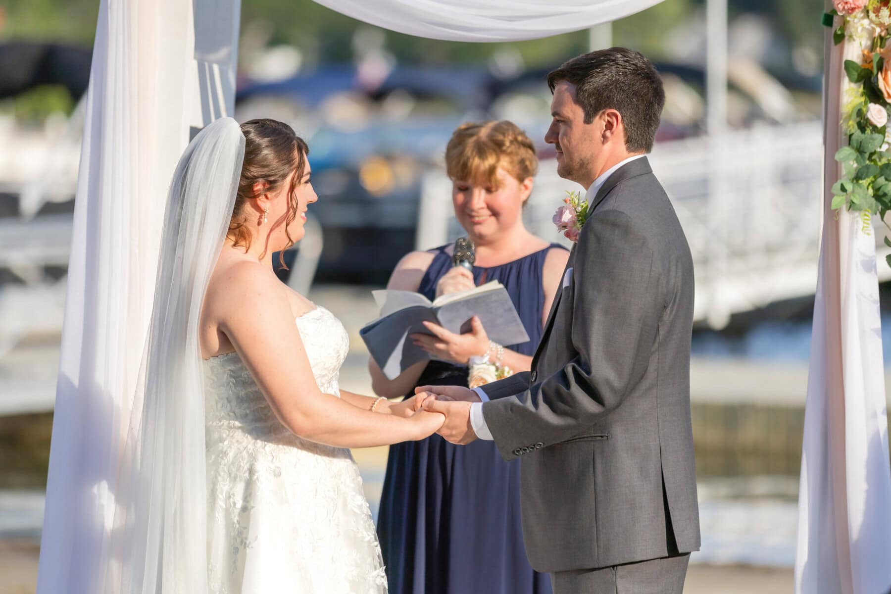 Stunning Wedding at Indian Ranch and Samuel Slater's Restaurant 40 A bride and groom hold hands during an outdoor wedding ceremony at Indian Ranch as an officiant reads from a book behind them.