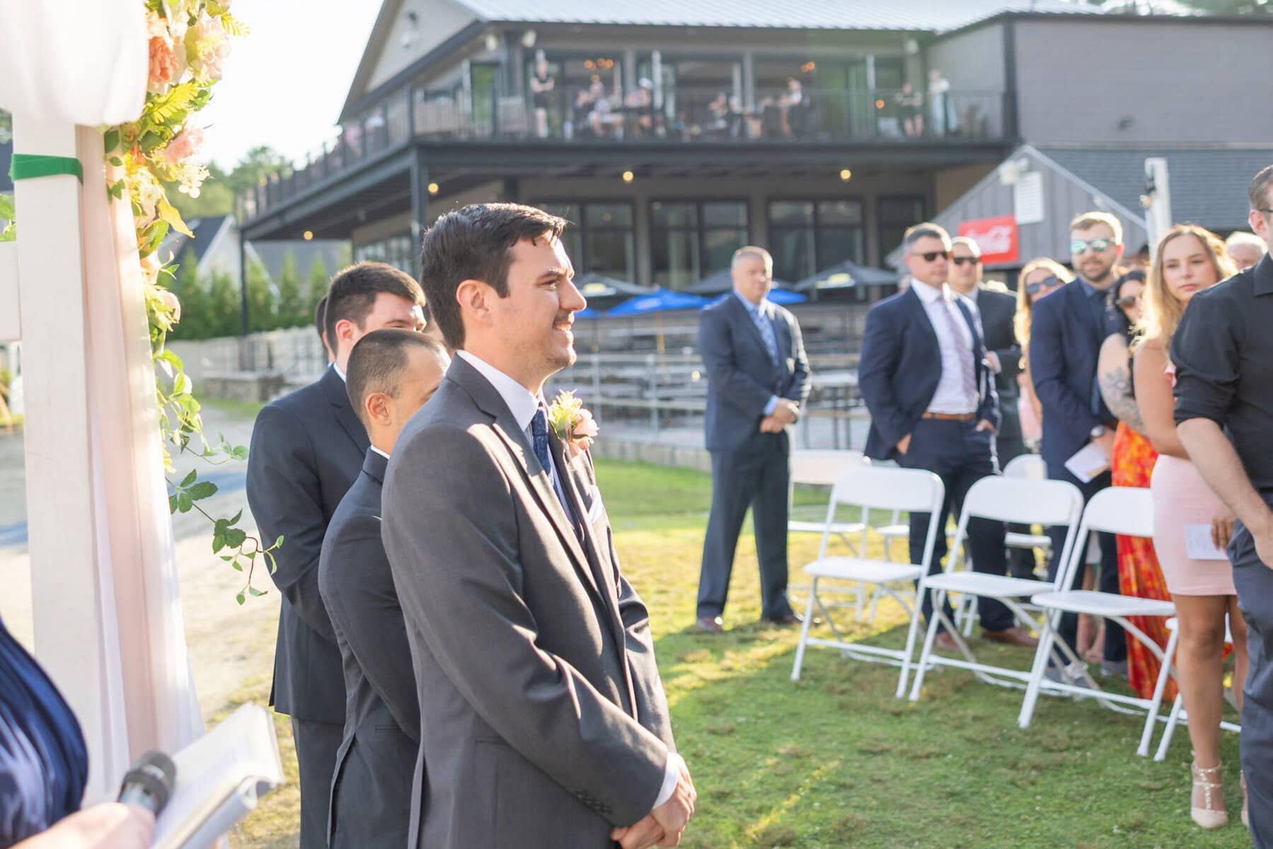 Stunning Wedding at Indian Ranch and Samuel Slater's Restaurant 36 A man in a suit stands at an Indian Ranch wedding ceremony, with guests gathered nearby on a sunny day.