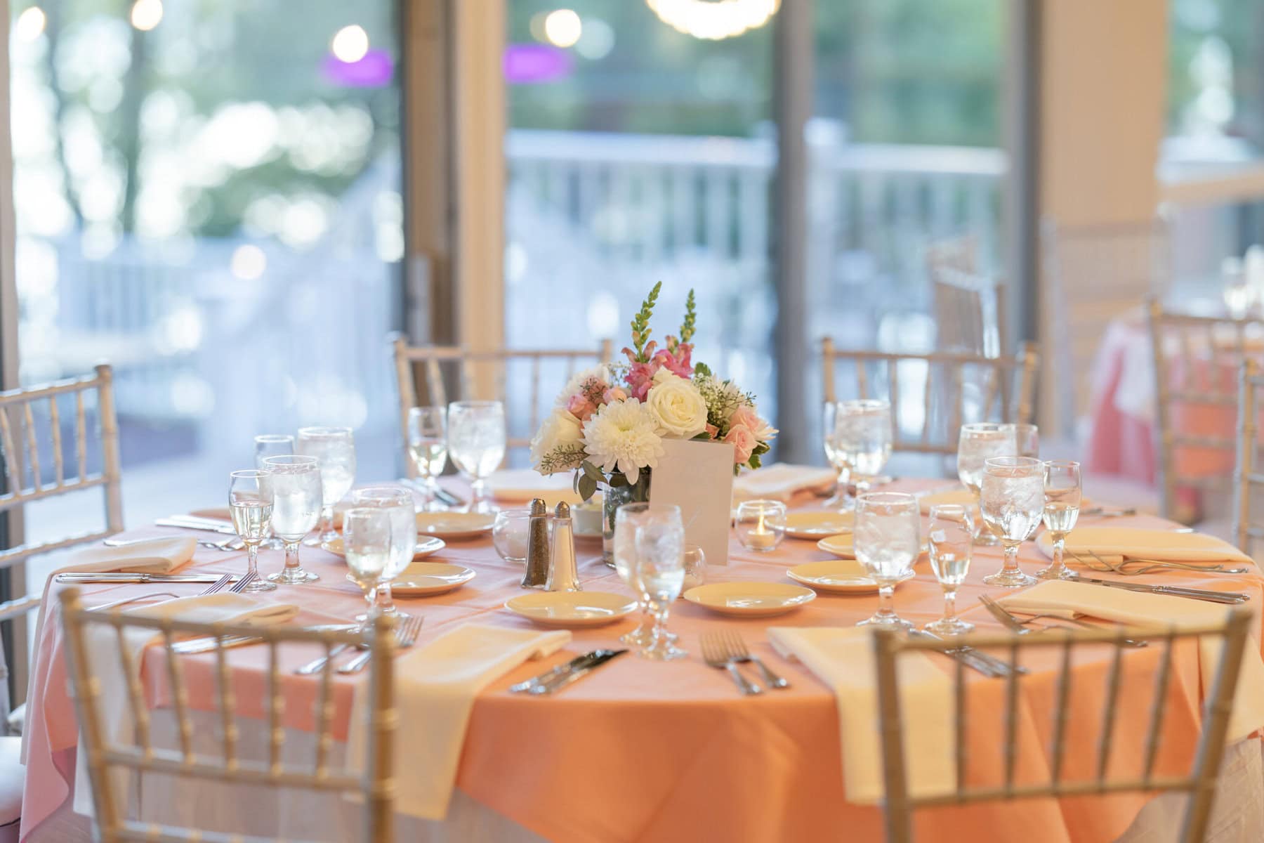 Beautiful Lake Pearl Wedding in Wrentham, MA 22 A round table set for a formal Lake Pearl Wedding in Wrentham MA with pink tablecloth, glassware, cutlery, and a floral centerpiece.