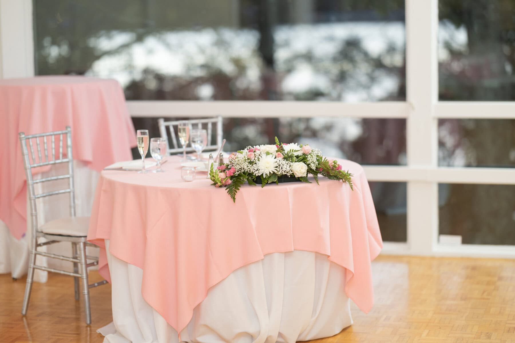 Beautiful Lake Pearl Wedding in Wrentham, MA 27 A round table with a pink and white tablecloth is set for two in a bright Lake Pearl Wedding venue in Wrentham, MA.