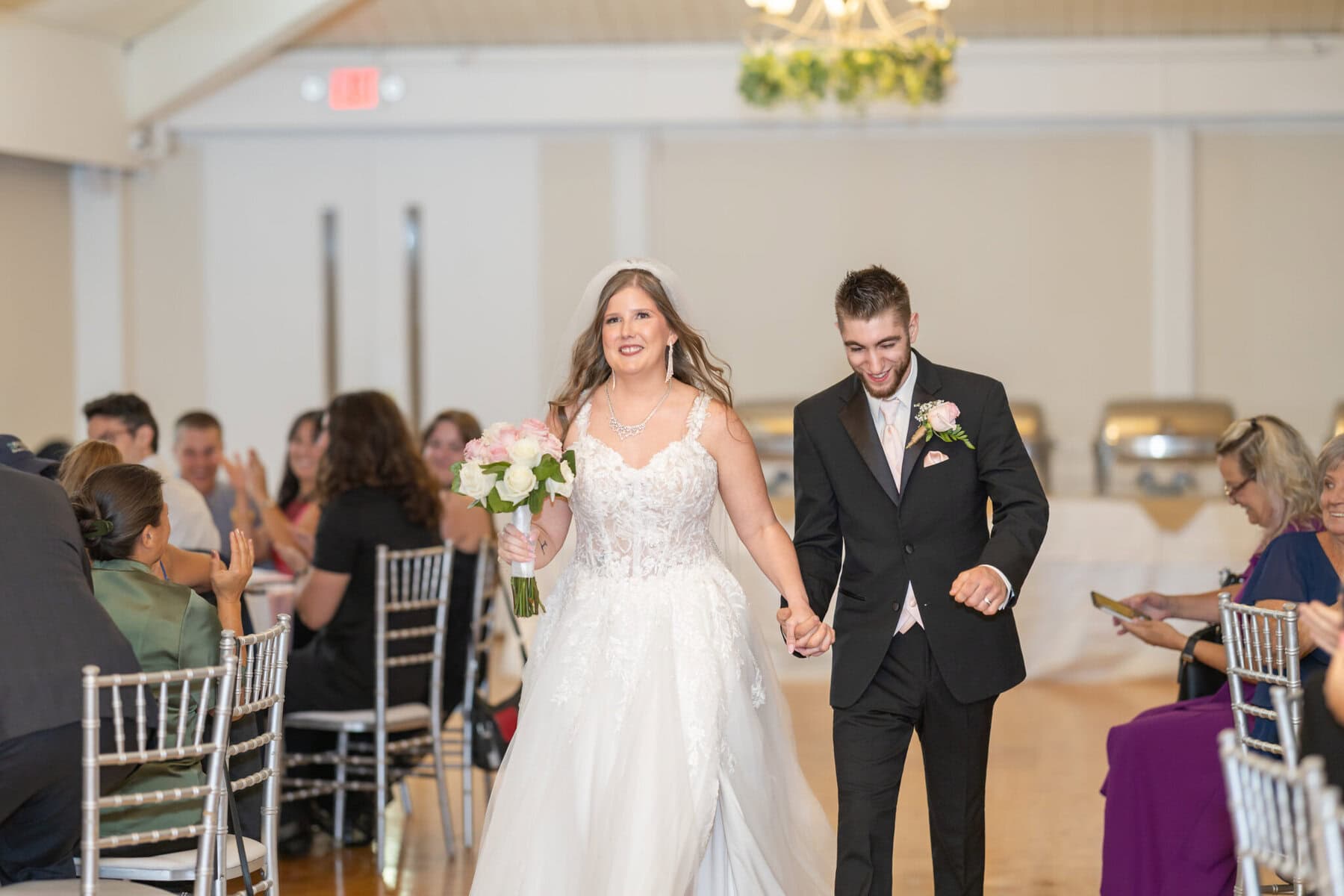 Beautiful Lake Pearl Wedding in Wrentham, MA 31 A bride in white and groom in black walk down the aisle at their Lake Pearl Wedding in Wrentham MA, as smiling guests watch and clap.
