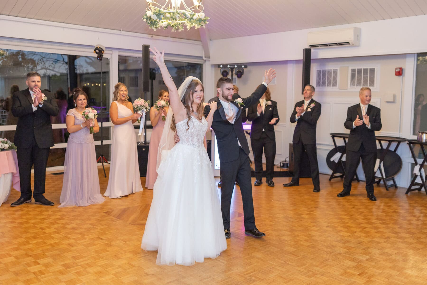 Beautiful Lake Pearl Wedding in Wrentham, MA 36 A bride and groom celebrate together at their Lake Pearl Wedding, with their wedding party applauding in a bright Wrentham MA reception hall.