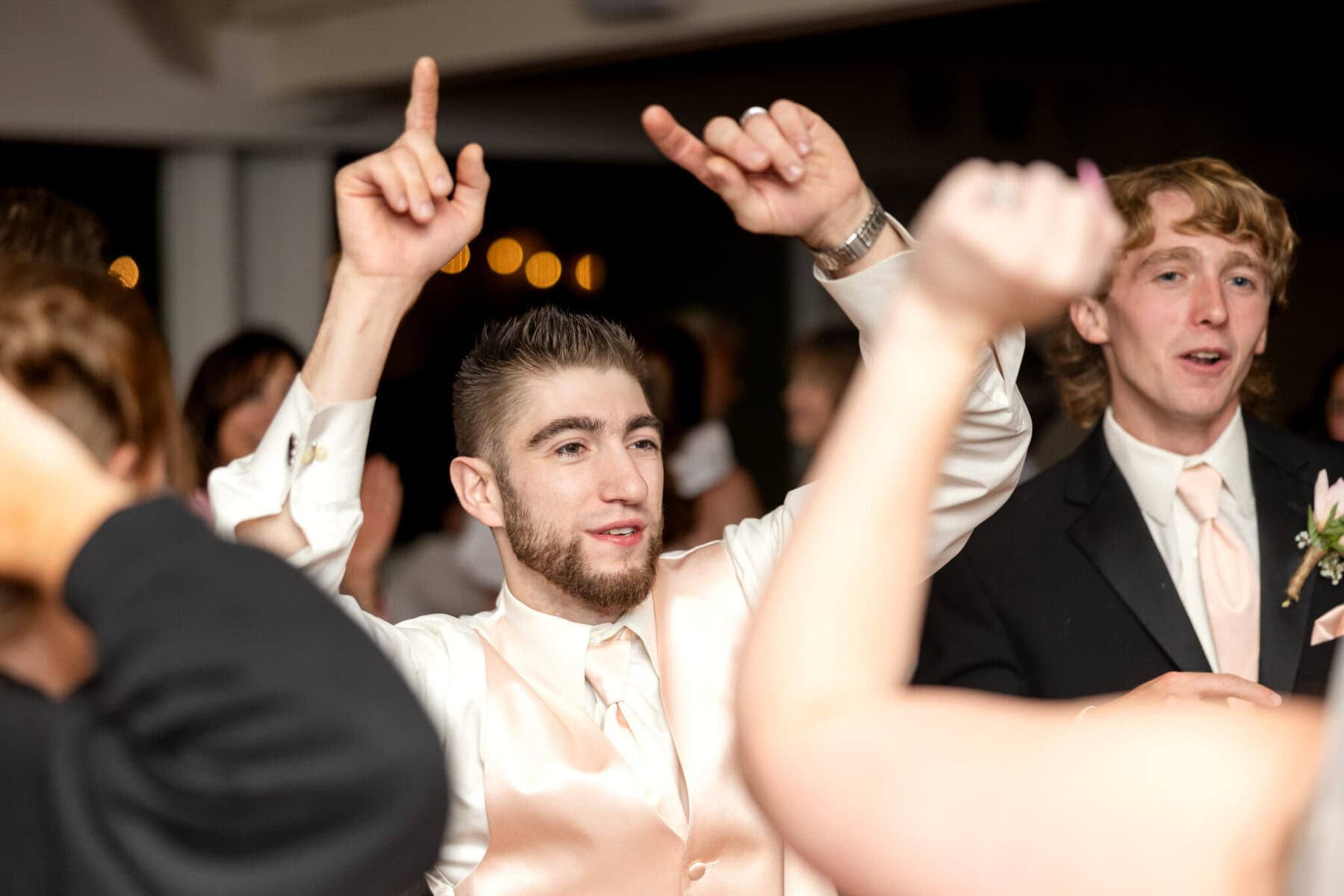 Beautiful Lake Pearl Wedding in Wrentham, MA 38 A man in a light vest and tie raises both arms while dancing at a Lake Pearl Wedding in Wrentham MA, with guests celebrating around him.