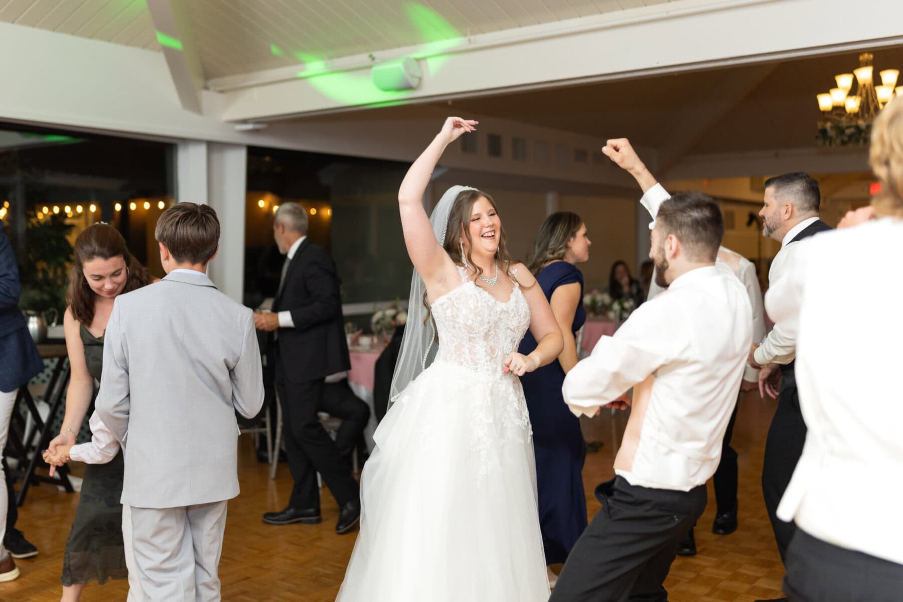 Beautiful Lake Pearl Wedding in Wrentham, MA 41 A bride in a white gown dances, smiling, surrounded by guests on the Lake Pearl Wedding dance floor in Wrentham, MA.