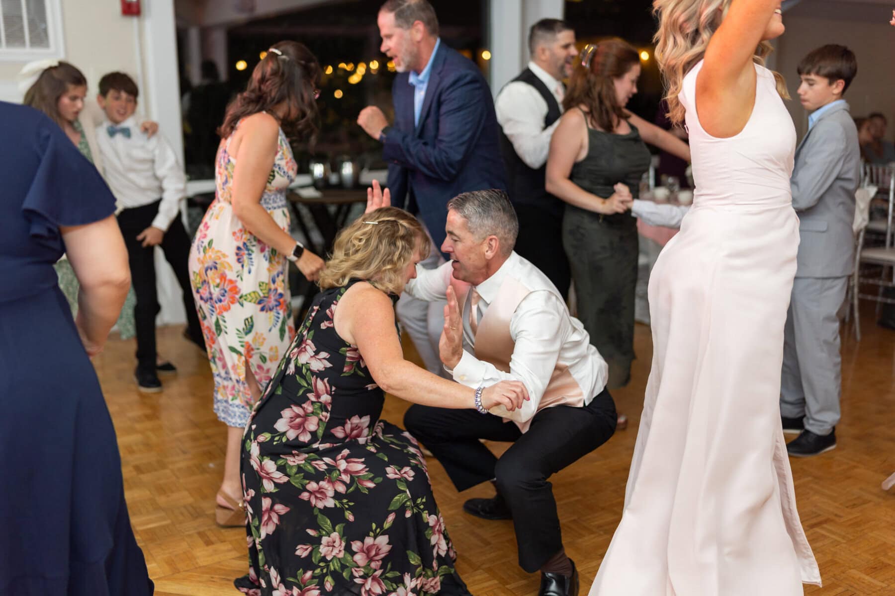 Beautiful Lake Pearl Wedding in Wrentham, MA 44 A group of people dressed formally dance energetically on a wooden floor at a Lake Pearl Wedding celebration in Wrentham MA.