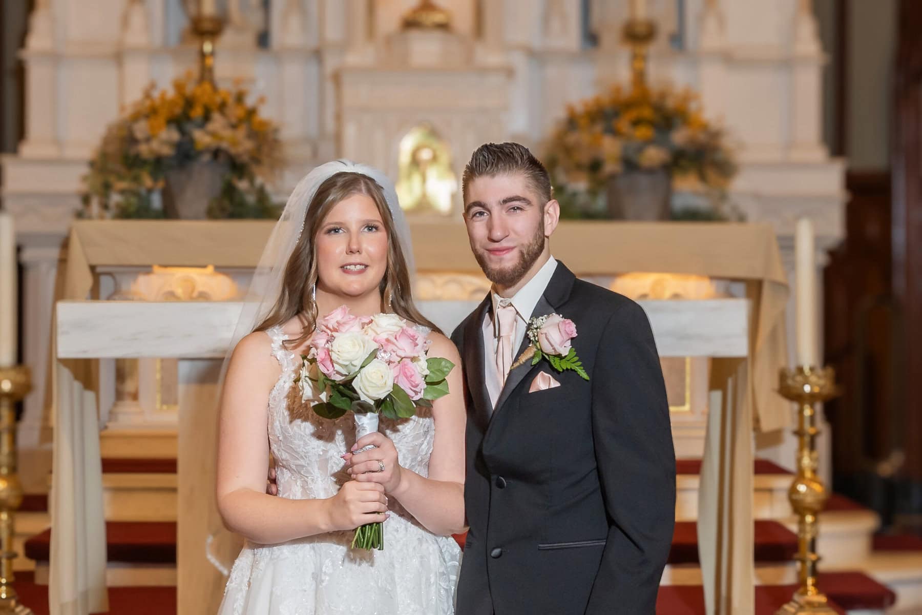 Wedding At St. Mary's Church in North Attleborough 5 A bride and groom stand together holding flowers at the altar of St. Mary's Church in North Attleborough on their wedding day.