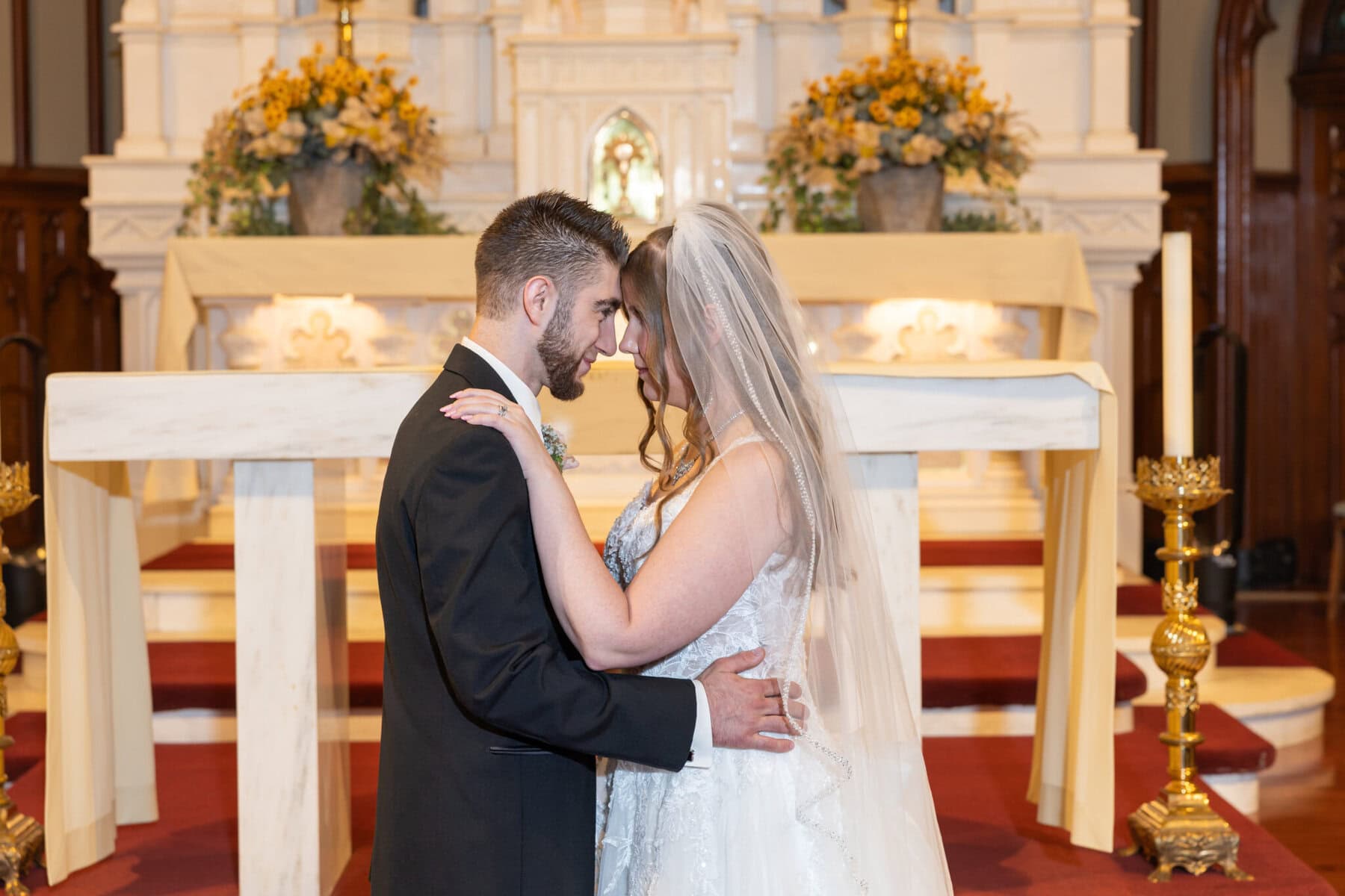 Wedding At St. Mary's Church in North Attleborough 4 A bride and groom stand close together, touching foreheads at the altar in St. Mary's Church, North Attleborough.