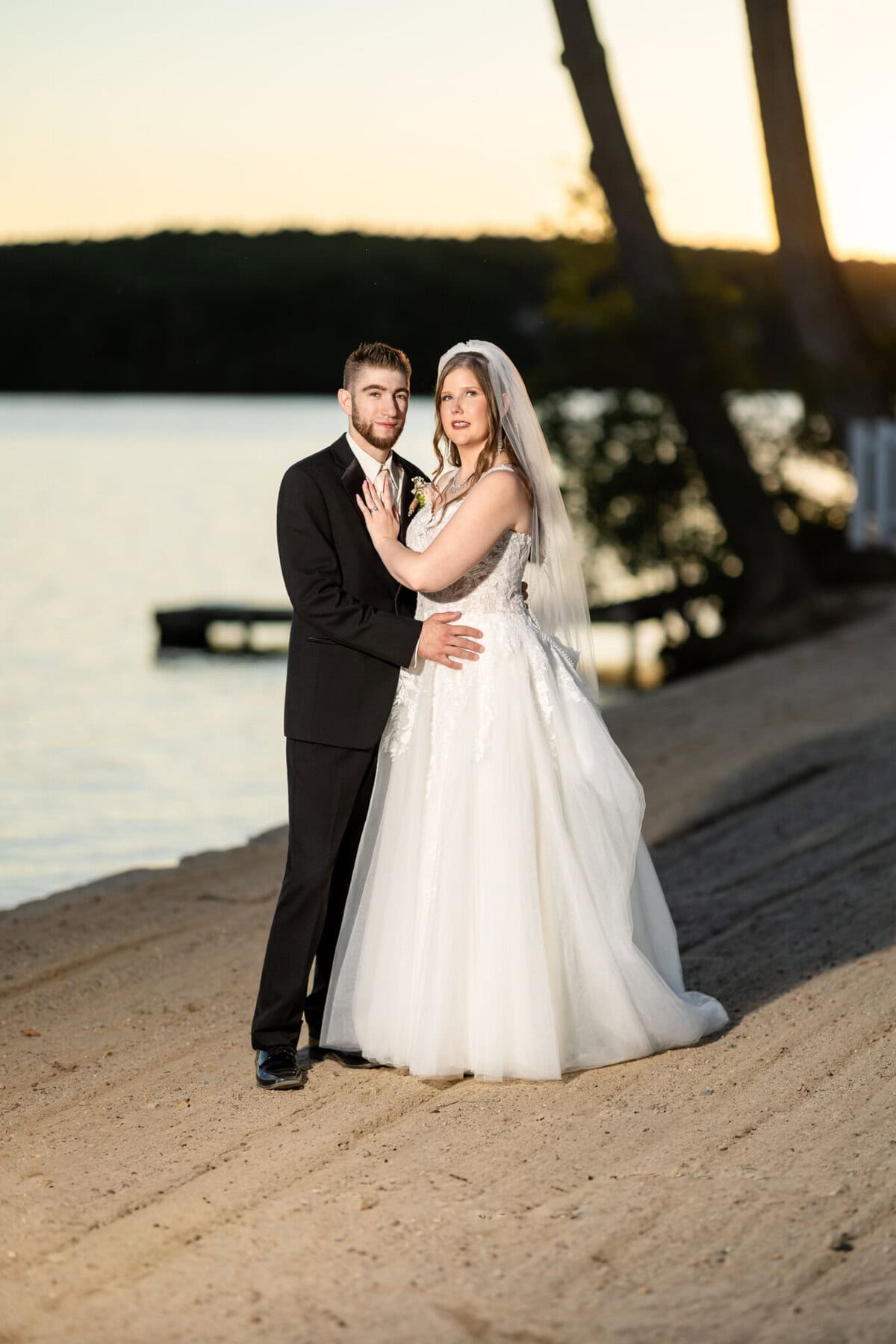 Beautiful Lake Pearl Wedding in Wrentham, MA 7 A bride and groom pose together on the sandy lakeshore at sunset during their elegant Lake Pearl Wedding in Wrentham MA.