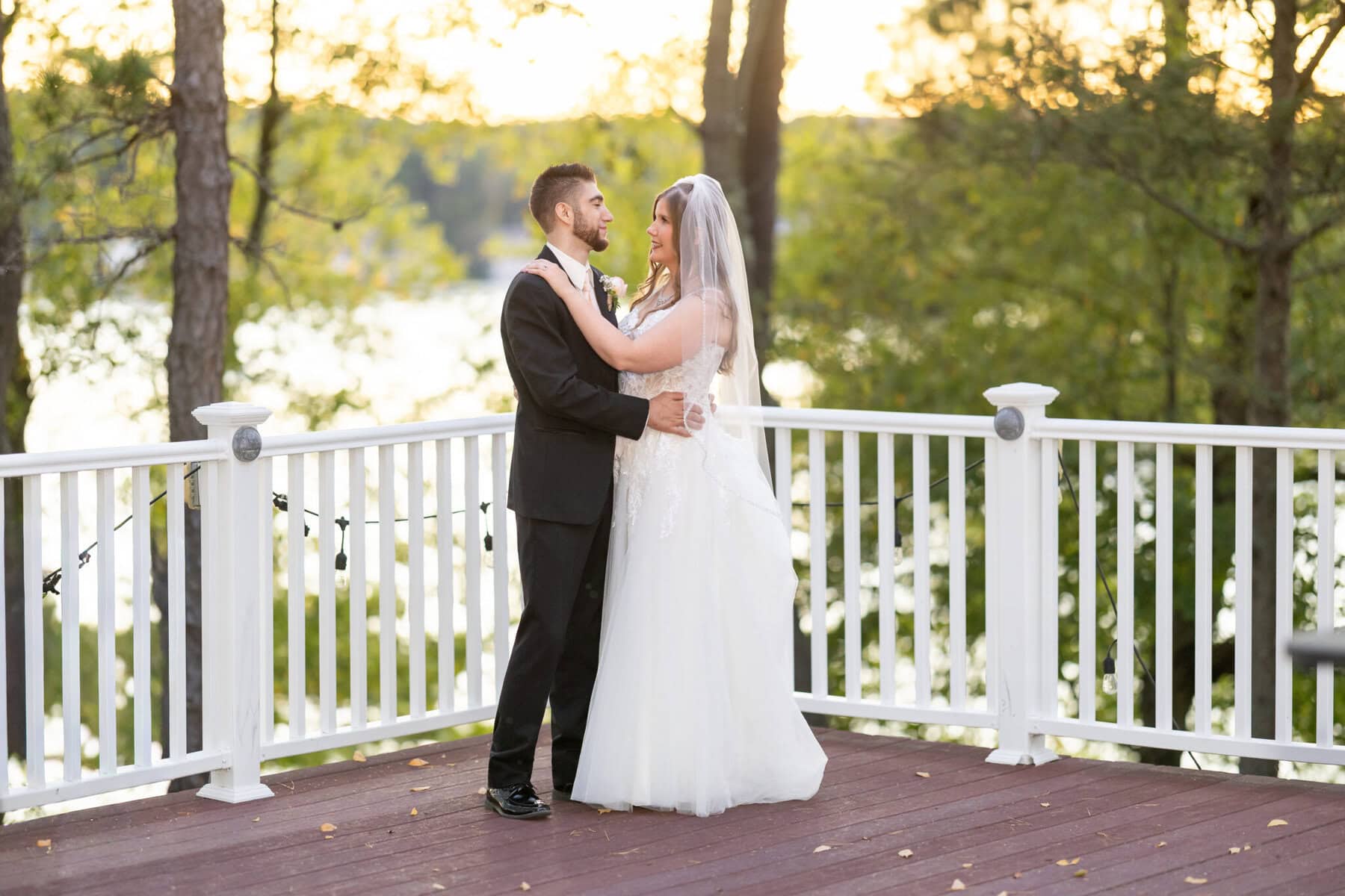Beautiful Lake Pearl Wedding in Wrentham, MA 10 A bride and groom smile at each other on a wooden deck at sunset during their Lake Pearl Wedding in Wrentham, MA.