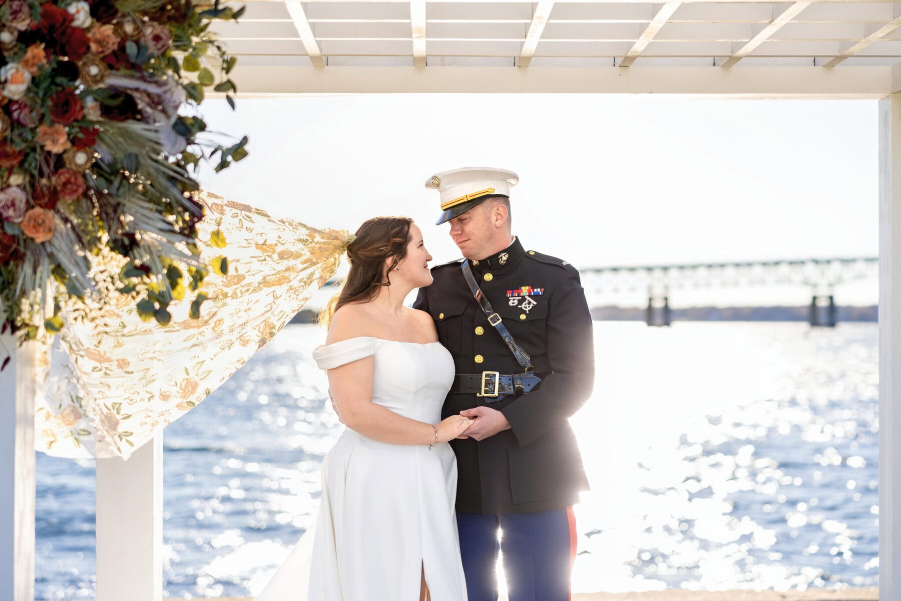 Wedding at the Newport Naval Station Officers' Club 47 A bride and groom in uniform stand hand in hand under an arch by the water at their Newport Naval Station wedding.