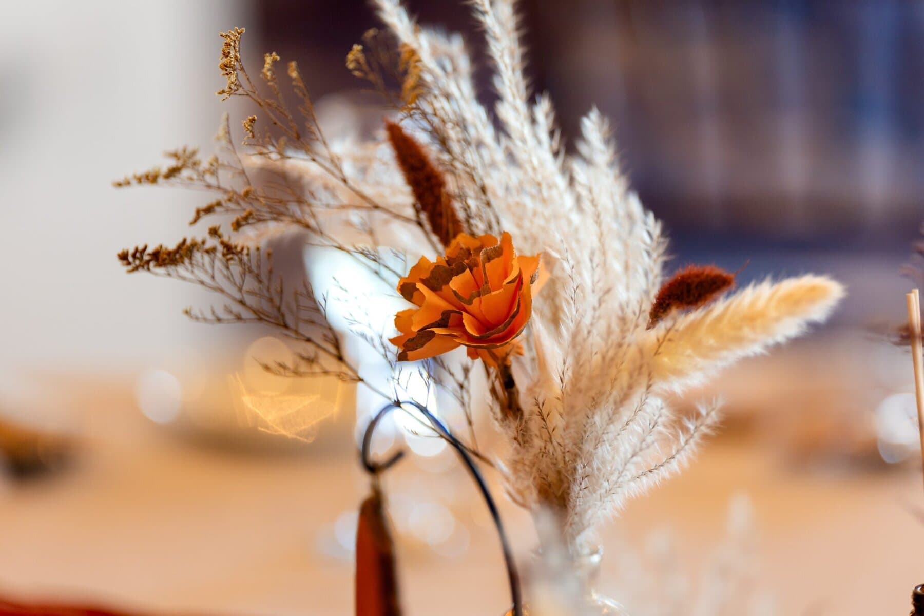 Wedding at the Newport Naval Station Officers' Club 61 A close-up of a wedding floral arrangement with an orange flower, dried grasses, and blurred background.