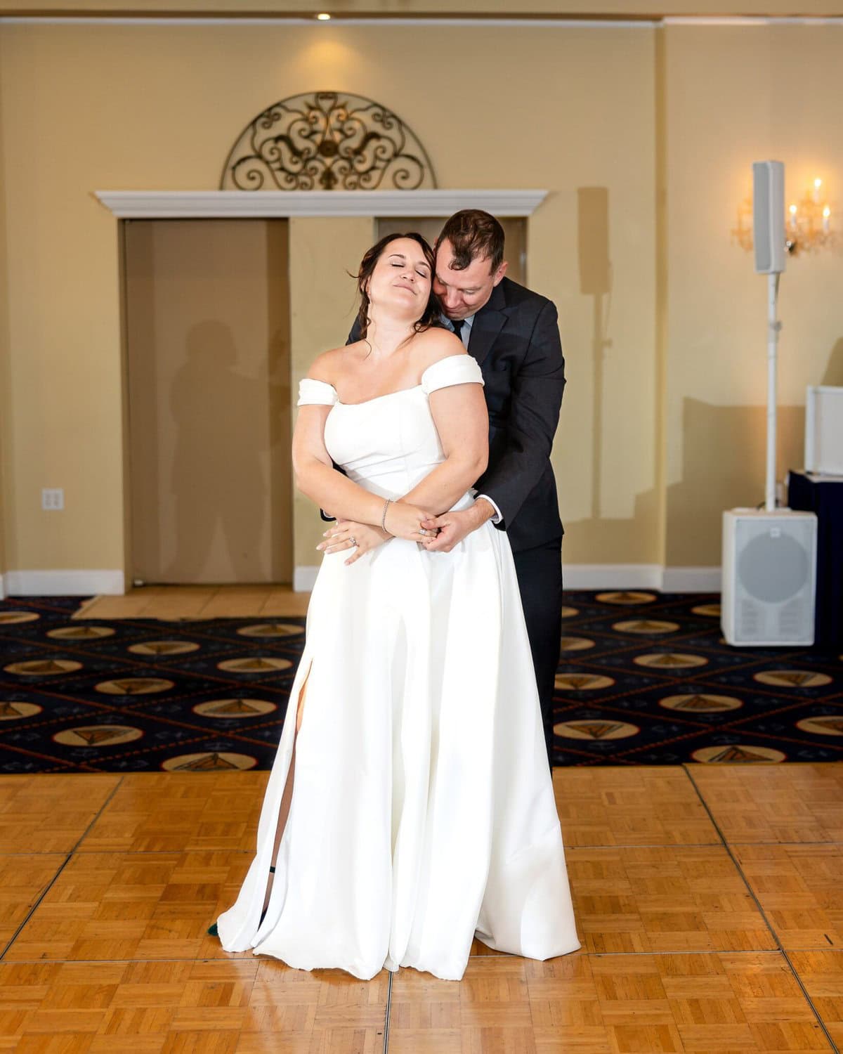 Wedding at the Newport Naval Station Officers' Club 69 A bride in a white gown and groom in a black suit embrace on a wooden dance floor at their elegant Newport wedding.