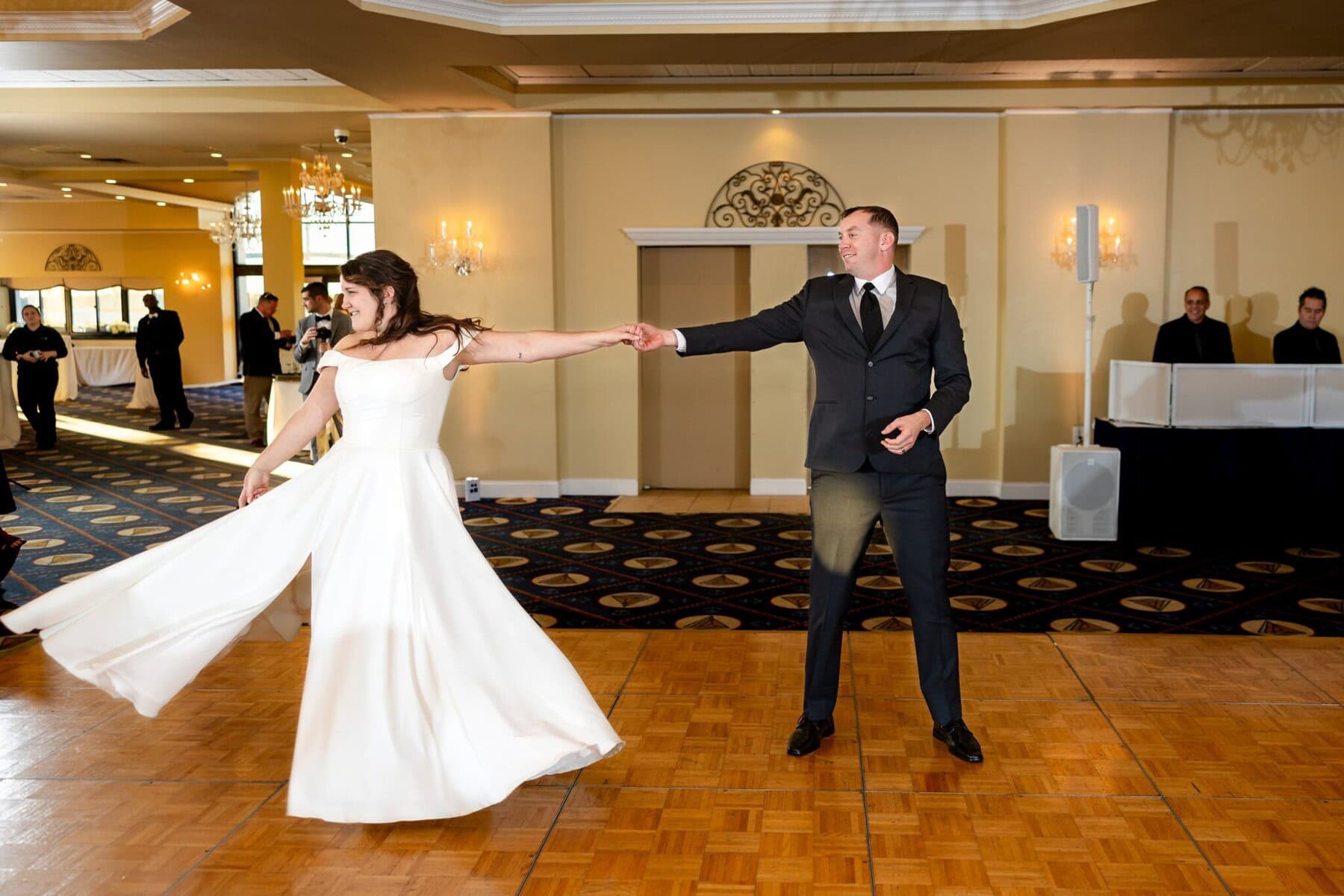 Wedding at the Newport Naval Station Officers' Club 70 A bride and groom dance on a wooden floor at the Officers' Club, celebrating their wedding as guests look on in the bright hall.