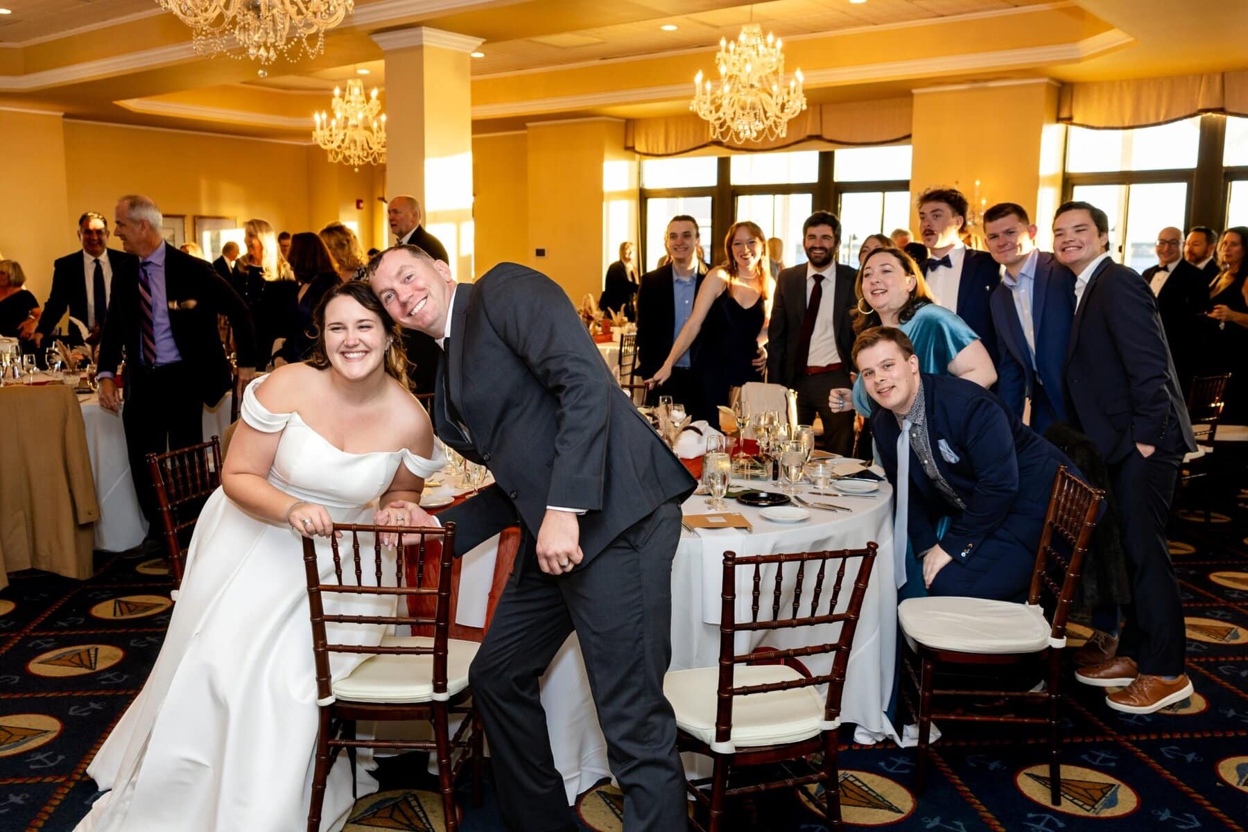 Wedding at the Newport Naval Station Officers' Club 73 A bride, groom, and guests in formal attire smile and pose at a Newport Naval Station Officers' Club wedding reception in a decorated banquet hall.