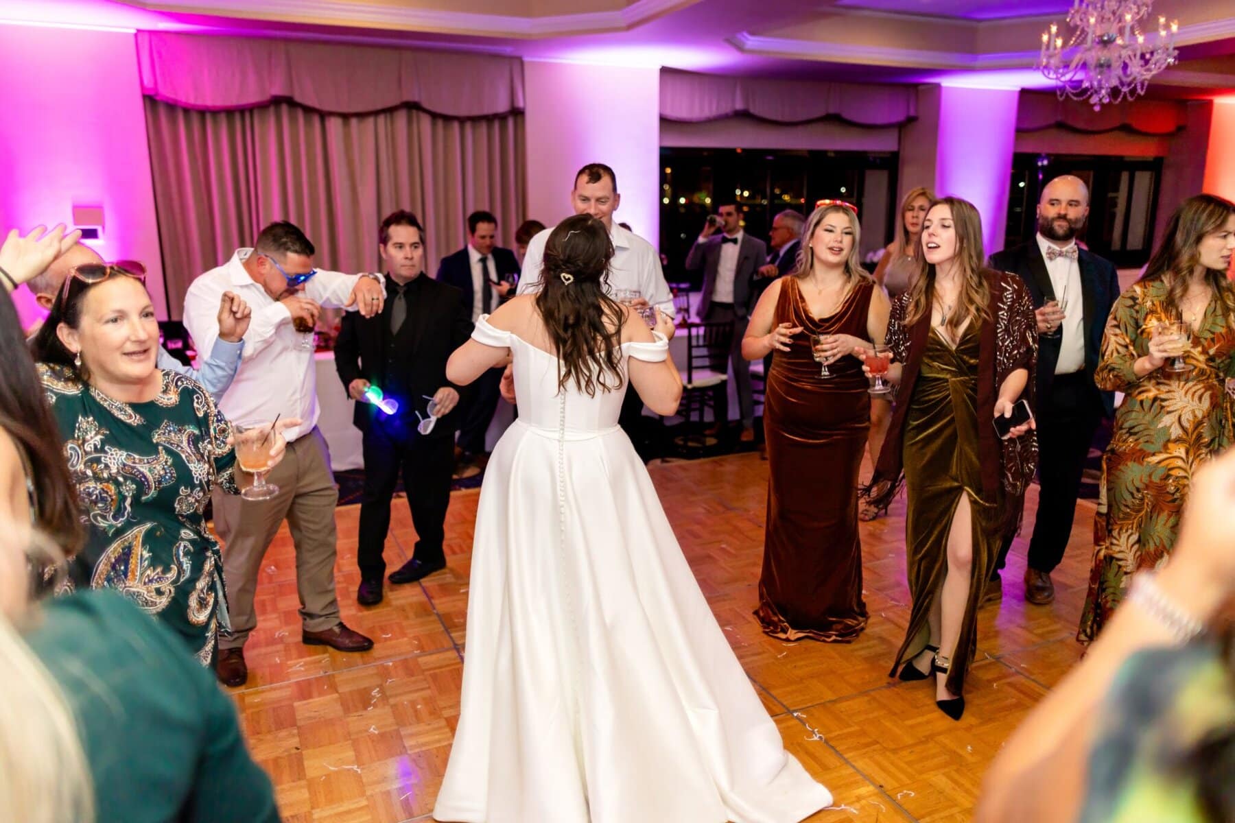 Wedding at the Newport Naval Station Officers' Club 87 A bride in a white dress dances on a wooden floor at a lively Newport wedding, surrounded by guests in formal attire.