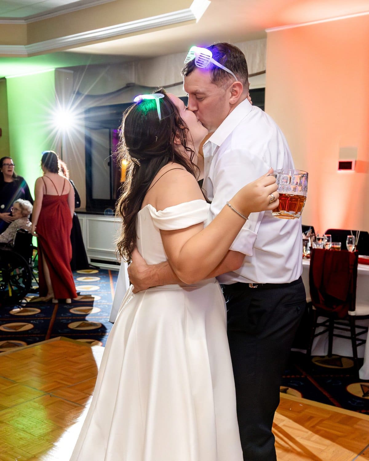 Wedding at the Newport Naval Station Officers' Club 88 A bride and groom wearing glowing glasses kiss on the dance floor at their Newport Naval Station wedding; the groom holds a glass mug.