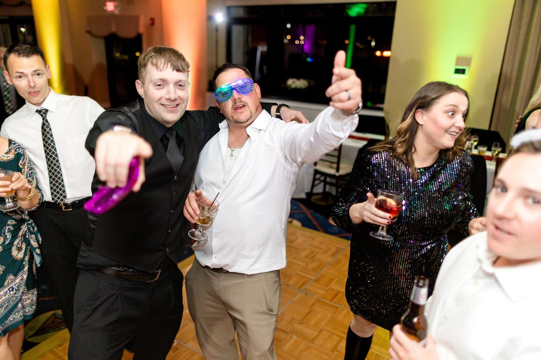 Wedding at the Newport Naval Station Officers' Club 90 A group of people dressed up, dancing and holding drinks at a wedding party at the Newport Naval Station Officers' Club with colorful lighting.