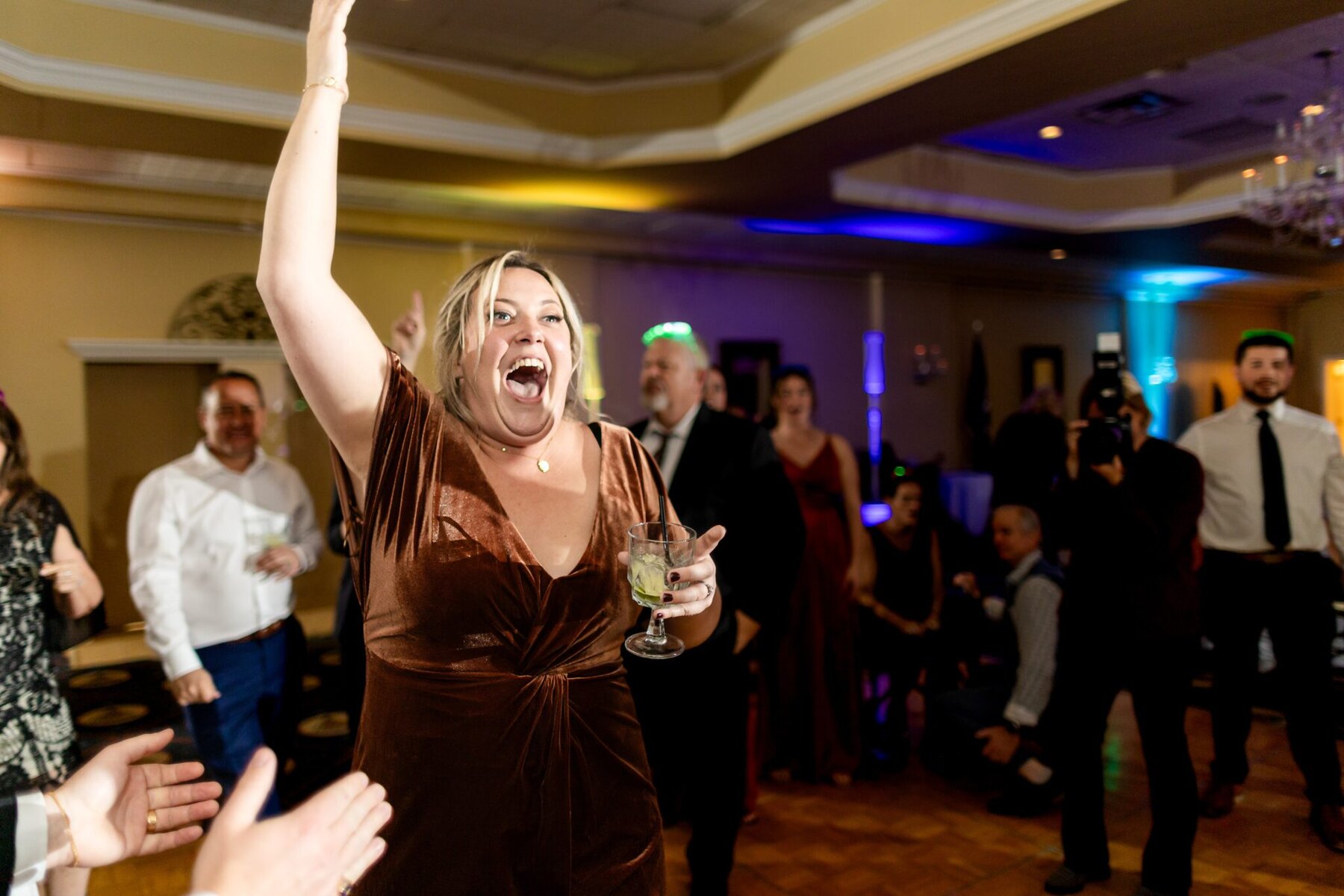 Wedding at the Newport Naval Station Officers' Club 96 A woman in a brown dress smiles and raises her drink at a lively wedding inside the Newport Naval Station Officers' Club.