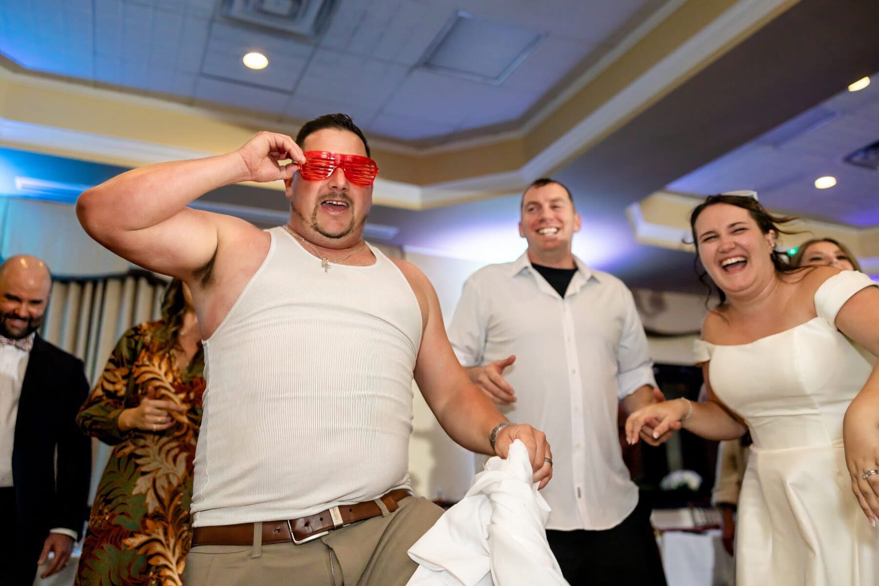 Wedding at the Newport Naval Station Officers' Club 106 A man in a tank top and red shutter shades poses playfully at a Newport Naval Station wedding, with guests laughing around him.