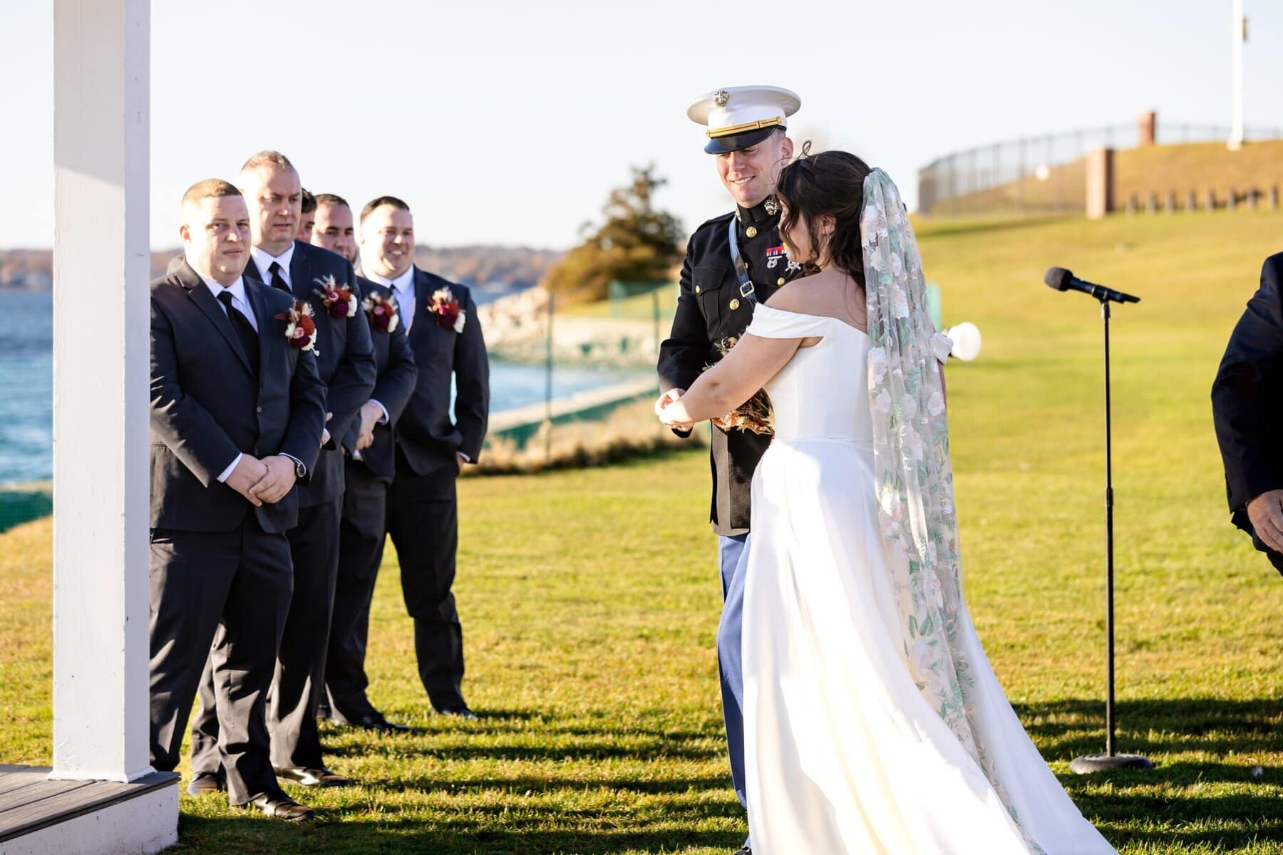 Wedding at the Newport Naval Station Officers' Club 33 A bride and groom stand together during an outdoor Officers' Club wedding at Newport Naval Station, with groomsmen and a microphone nearby.