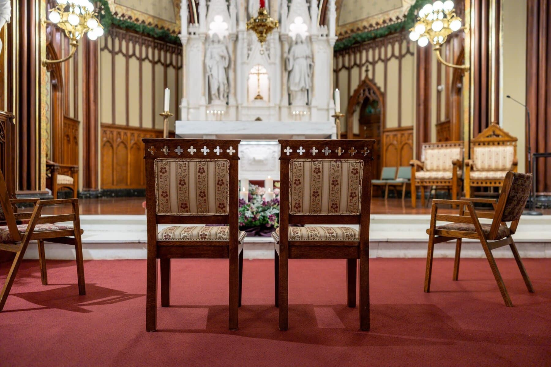 Wedding At the Transfiguration of the Lord Parish 7 Two ornate chairs face the altar, set for a Wedding ceremony in a church, with others around and the white-and-gold altar in the background.