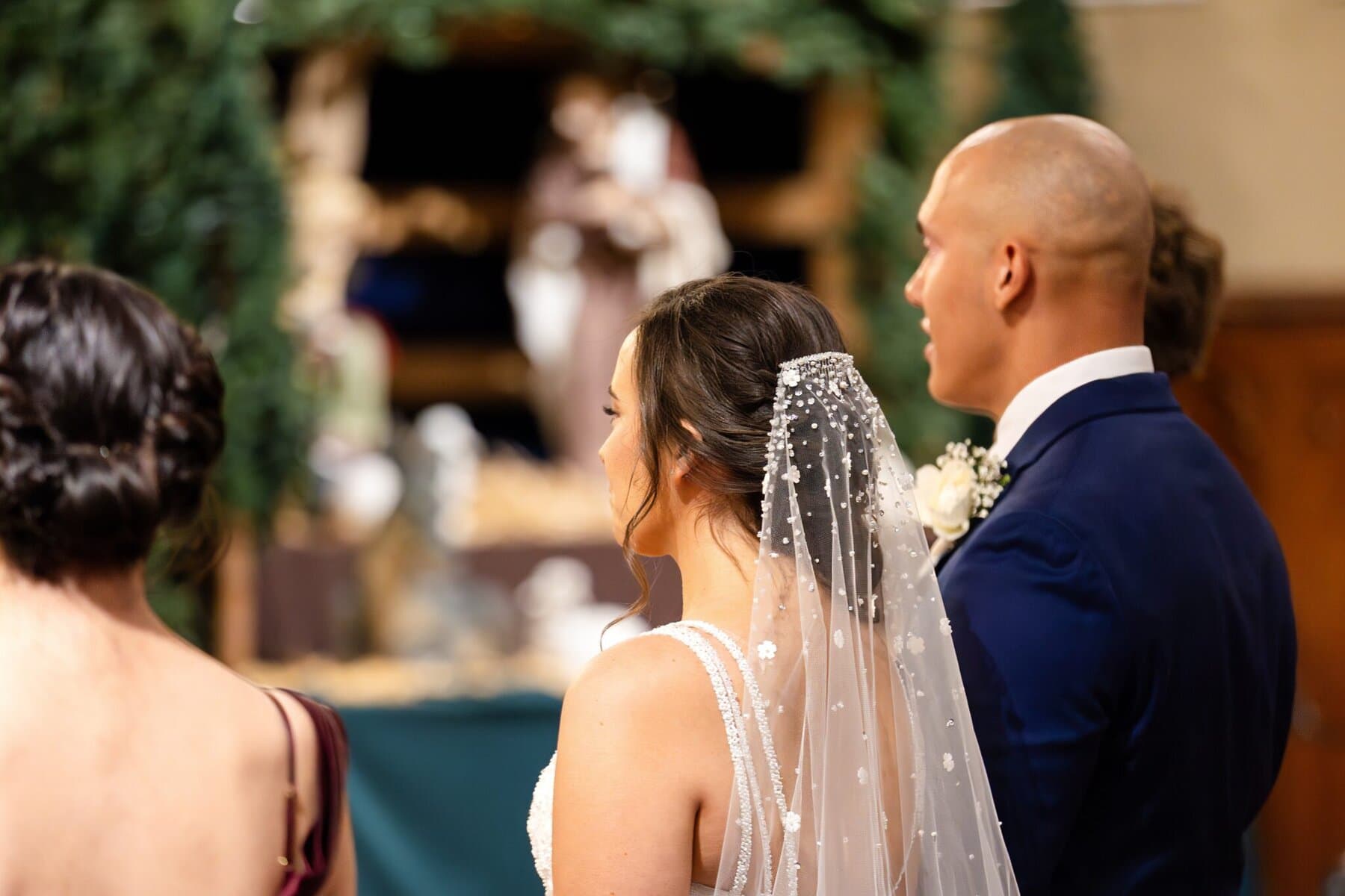 Wedding At the Transfiguration of the Lord Parish 32 A bride and groom stand side by side indoors at Transfiguration of the Lord Parish, with another woman standing in front of them.